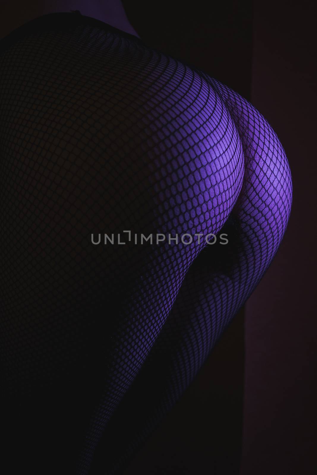 Back view of crop female with sexual ass in stockings in grid standing in darkness