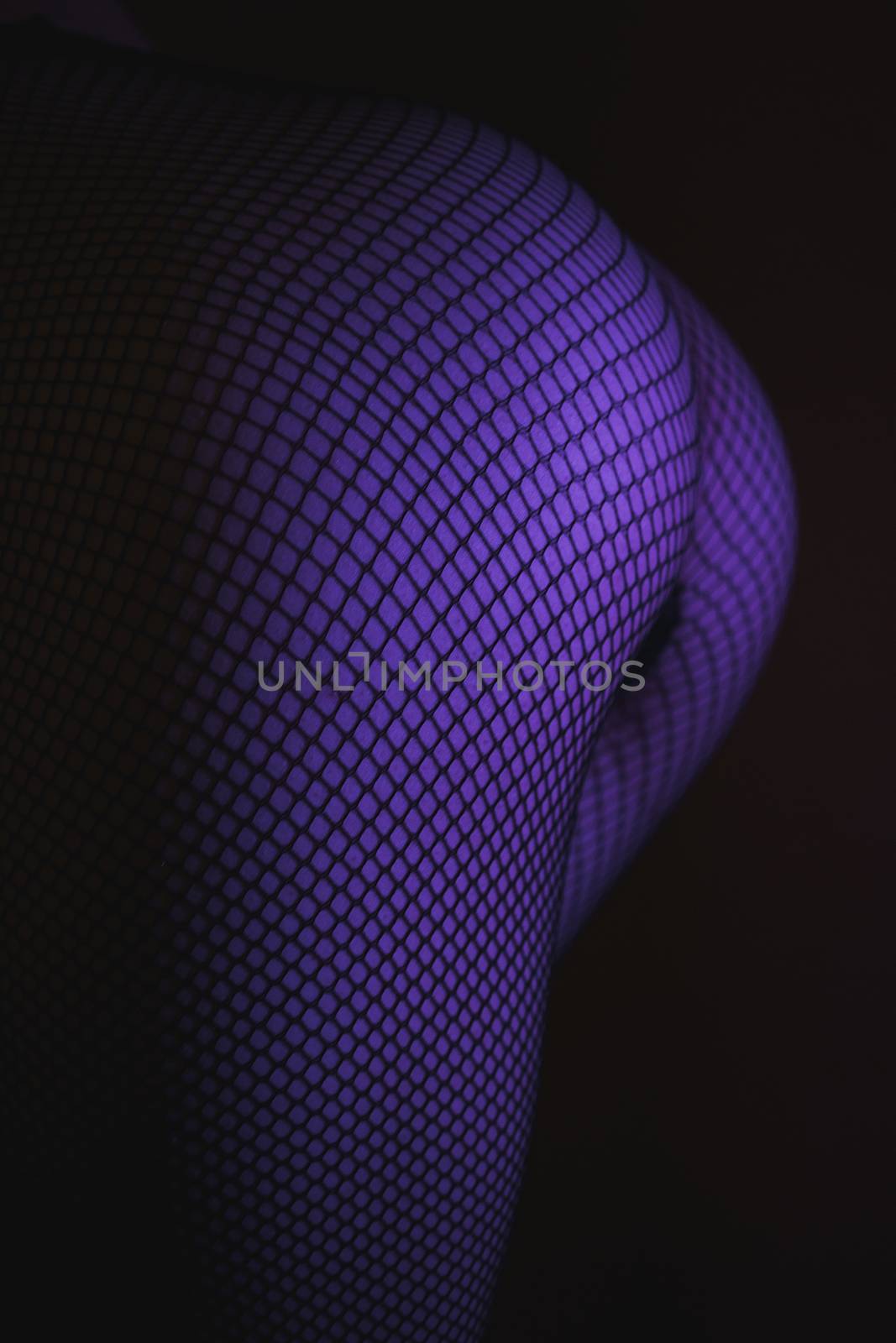 Back view of crop female with sexual ass in stockings in grid standing in darkness