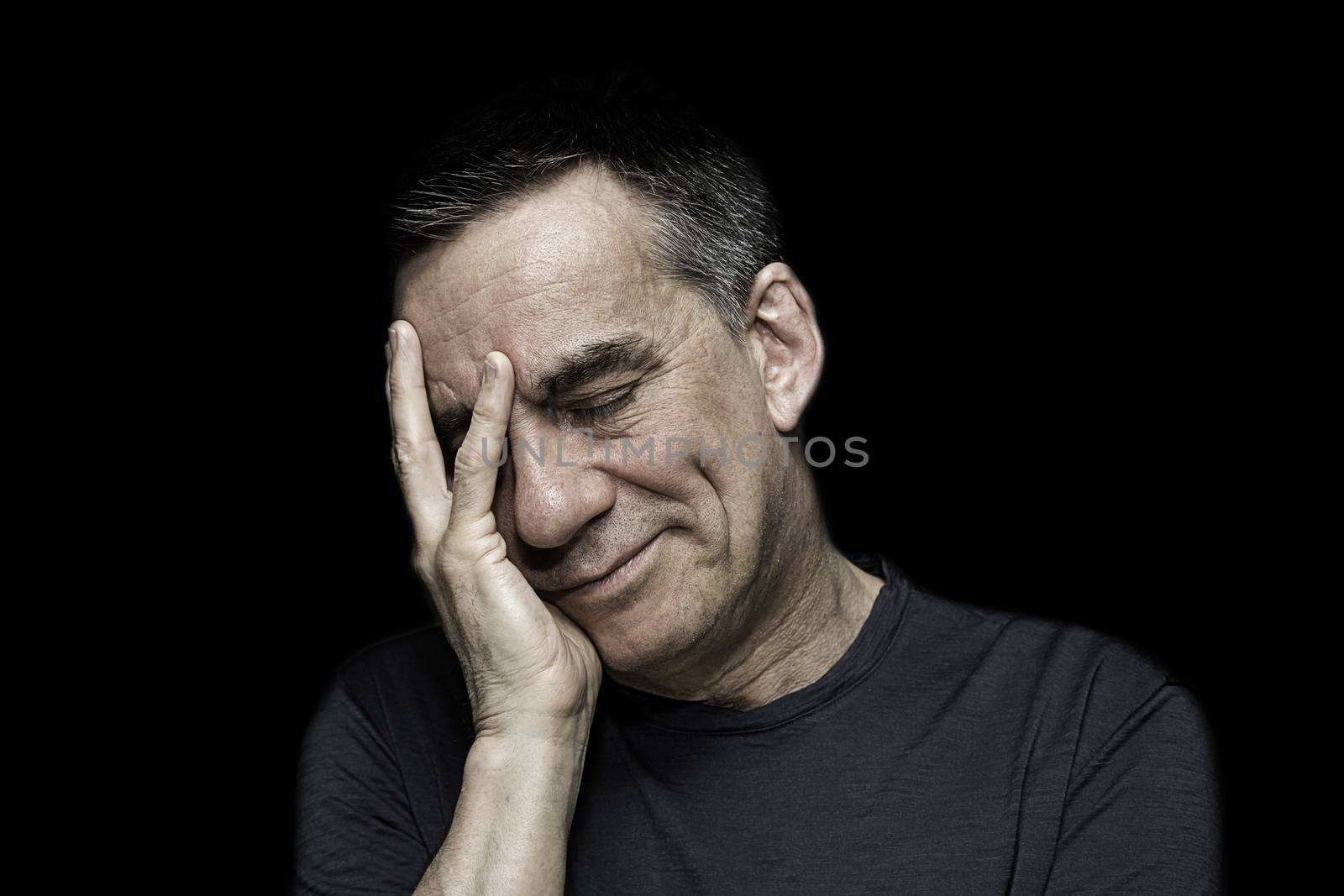 Closeup High Contrast Portrait of Sad Unhappy Man with Hand to Face on Black Background