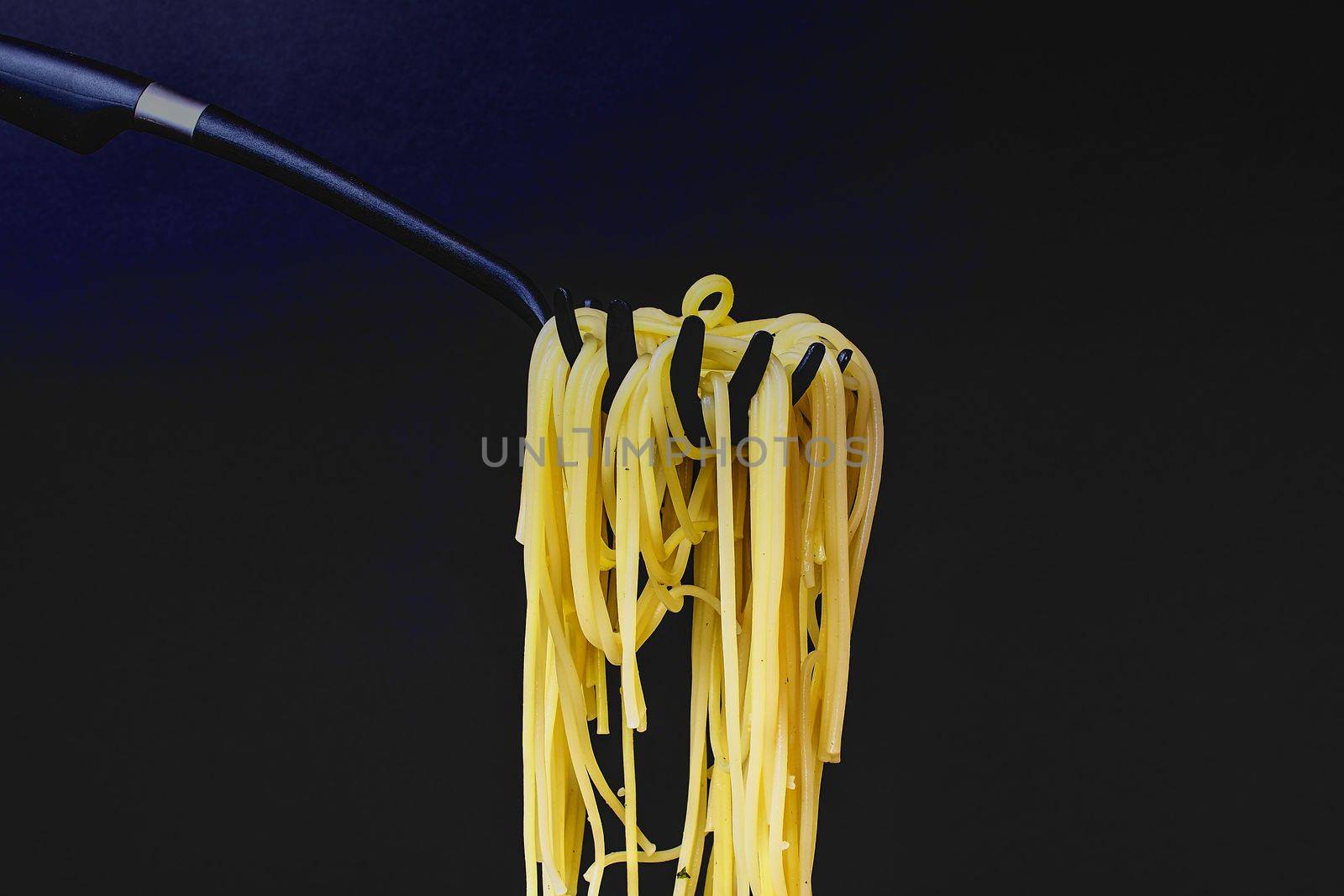 Cooked spaghetti on spaghetti spoon. Spaghetti on black background. Dark food photo. Copy space by roman_nerud