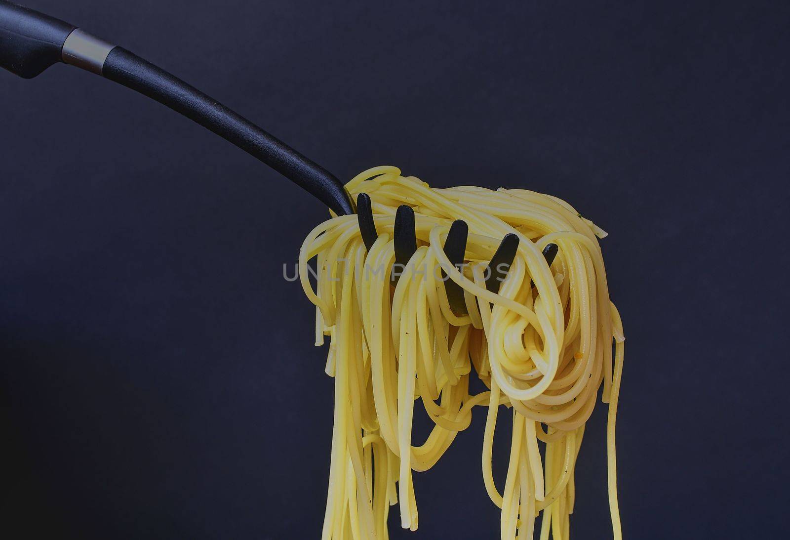 Cooked spaghetti on spaghetti spoon. Spaghetti on black background. Close-up. Dark food photo. Copy space.