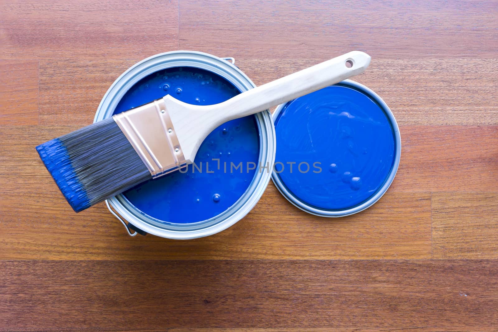 Top view of blue paint can and brush on top with cherry hardwood floor background