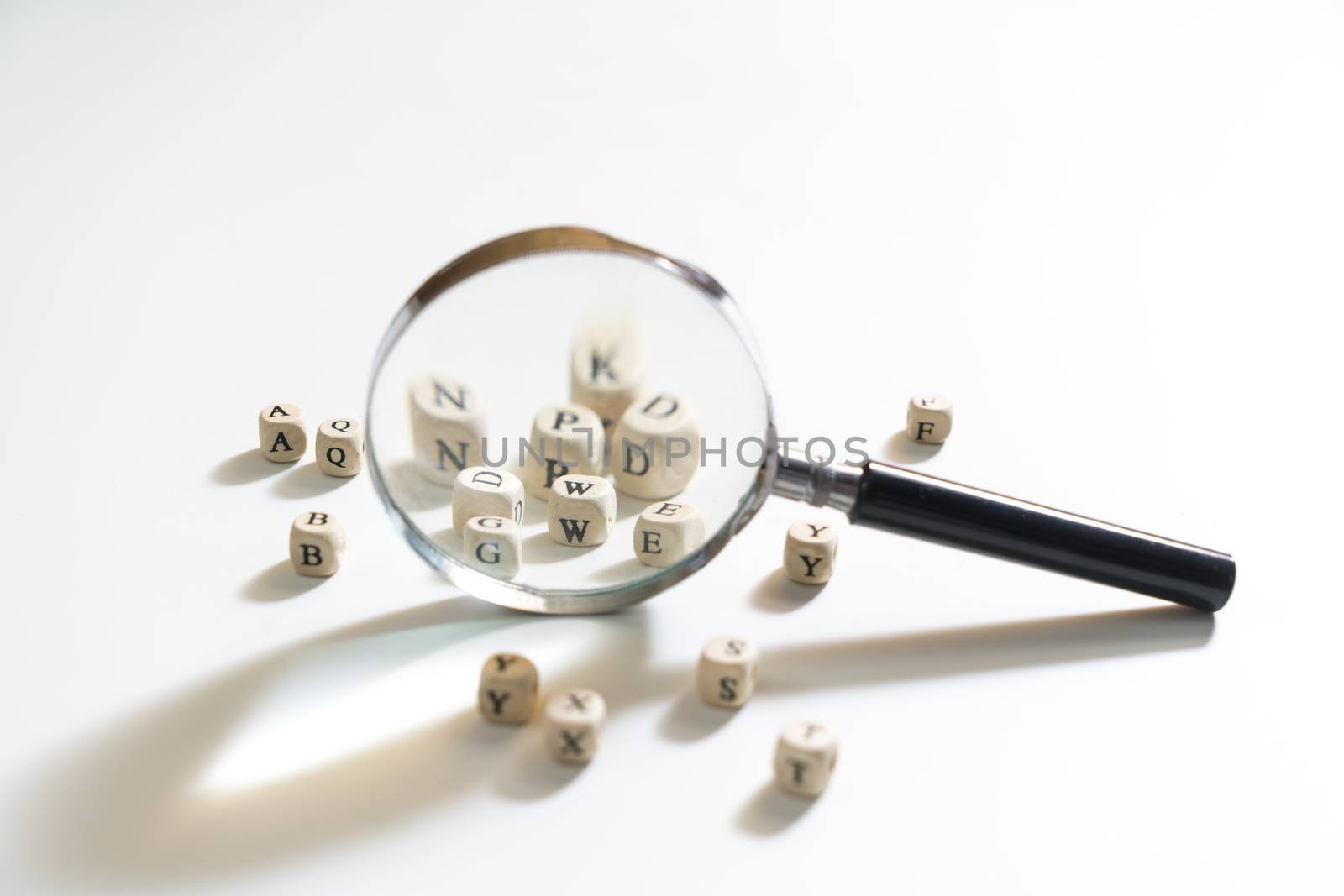 a magnifying glass between some letters of the alphabet on a white surface