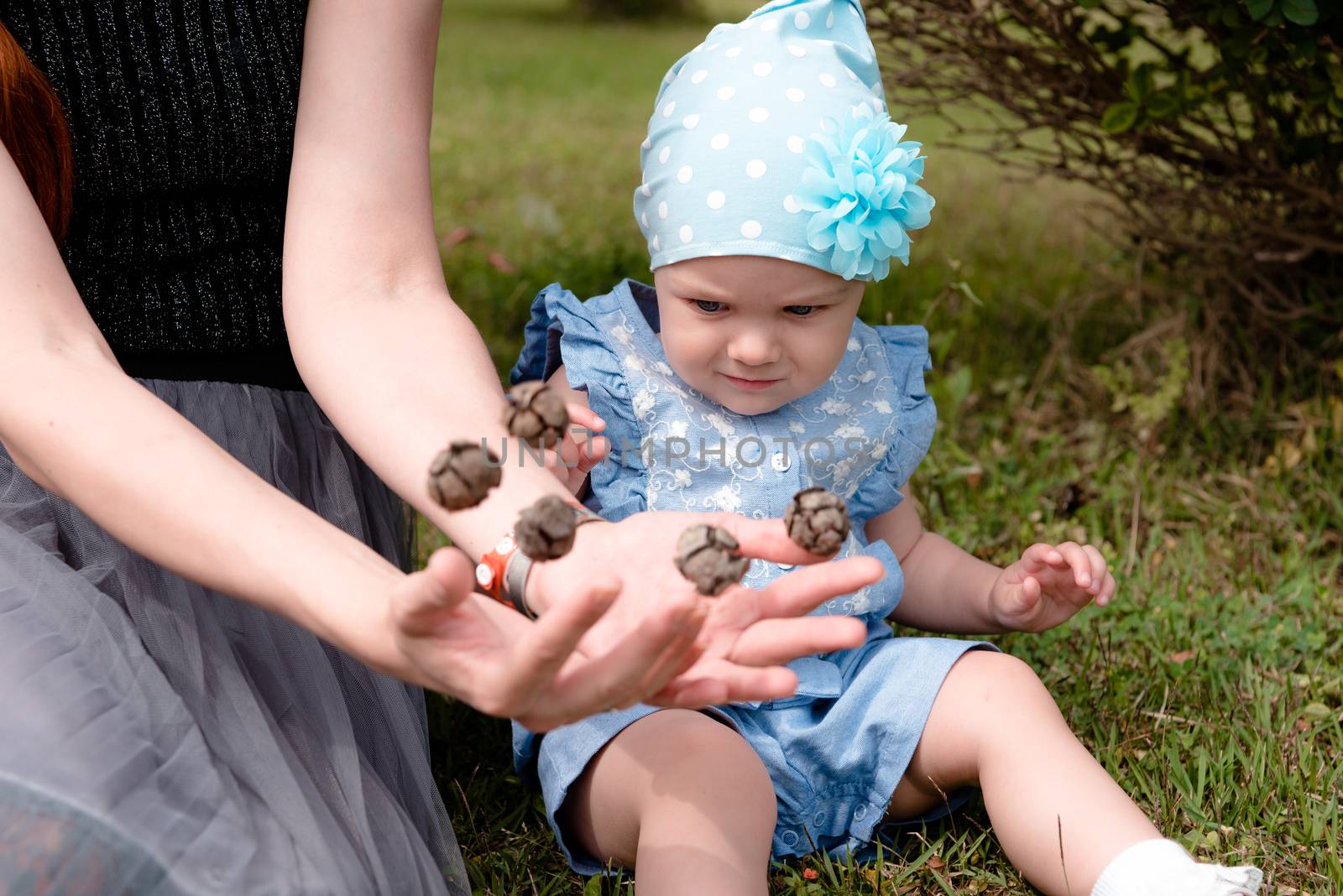 the little girl looks at the flying cones in the hands of her mother with distrust. they sit on the grass in the Park. the child has a blue suit and a hat.