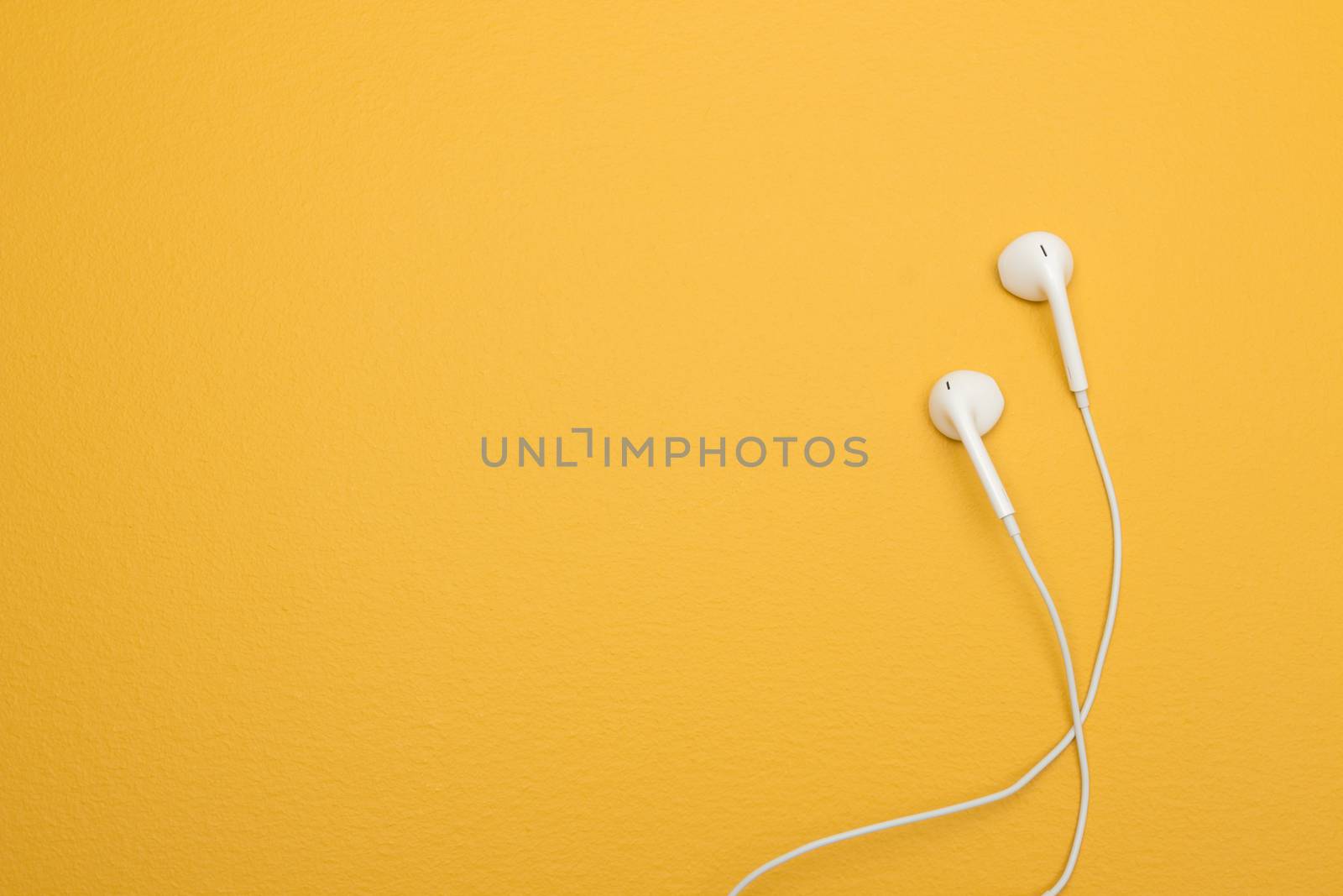 White earphones on yellow background with copy space by anikasalsera