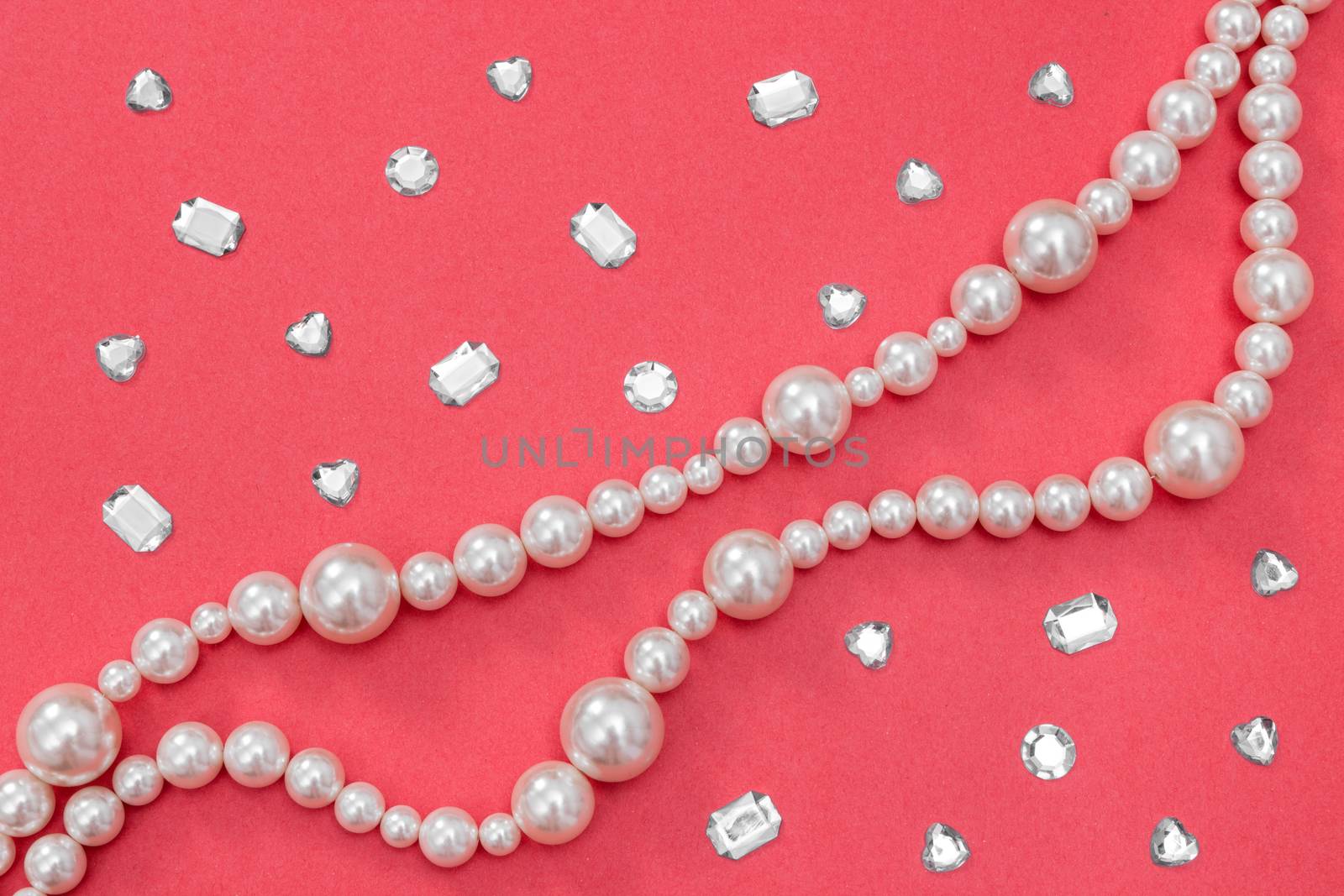 Pearl necklace and shiny gems on vivid pink background. Fashion background.