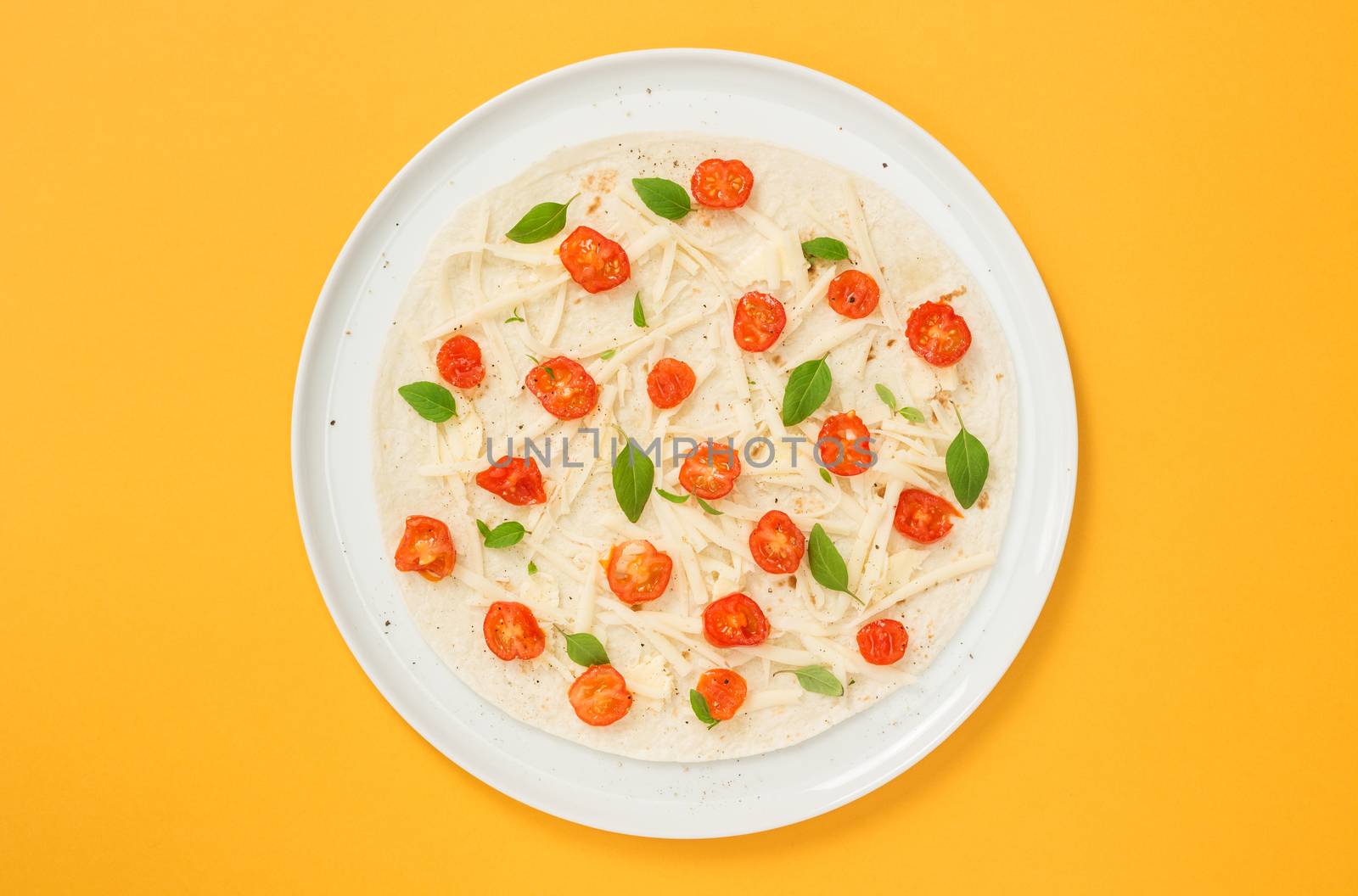 Tortilla preparation. Vegetarian tortilla with tomatoes, cheese and basil, on bright yellow background.