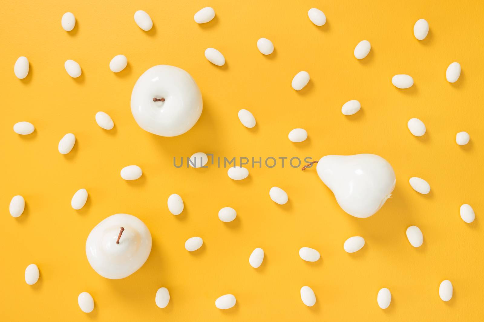 White chocolate candies and painted fruits on yellow background by anikasalsera