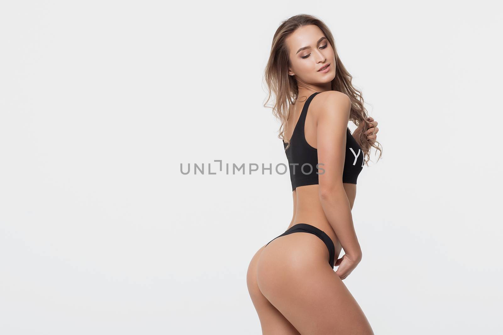 Side view of seductive young woman in black underwear standing with eyes closed in studio