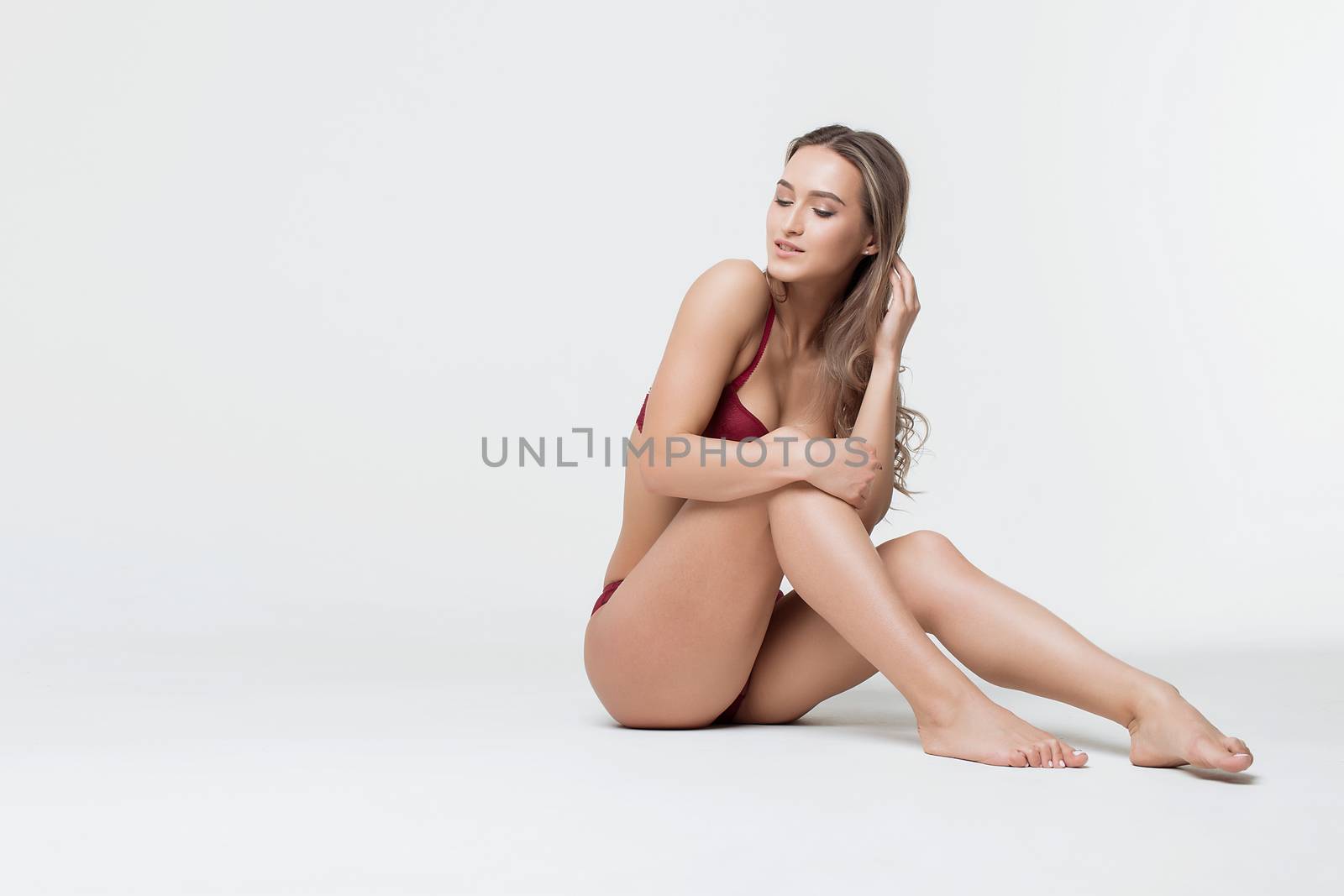 Studio shot of young sexy female sitting wearing underwear touching hair with eyes closed in studio with white background
