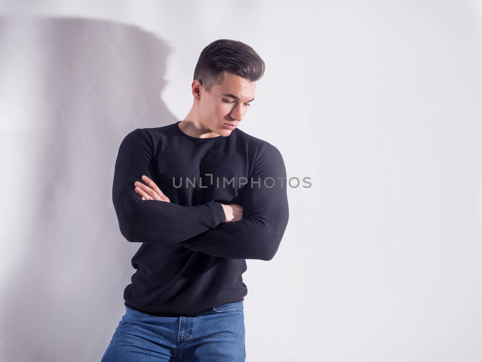 Handsome young muscular man looking down in studio shot, on grey background in studio