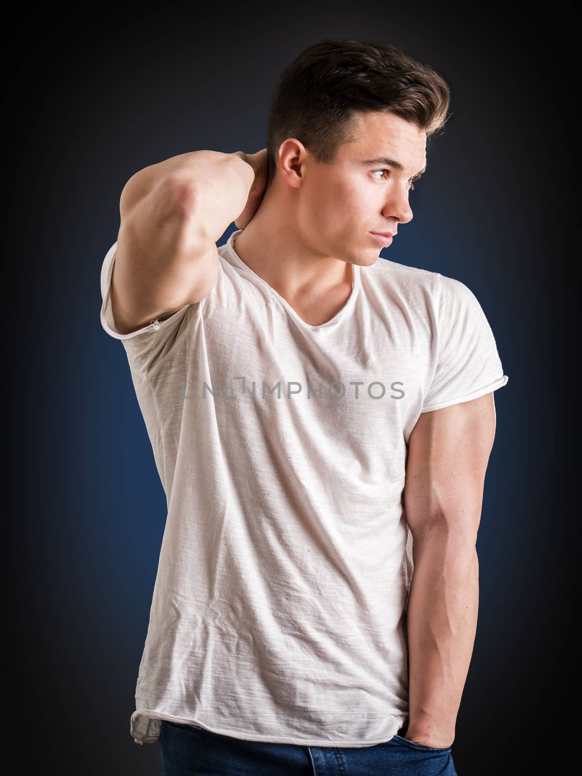 Handsome young muscular man looking down to a side, in studio shot over neutral dark background