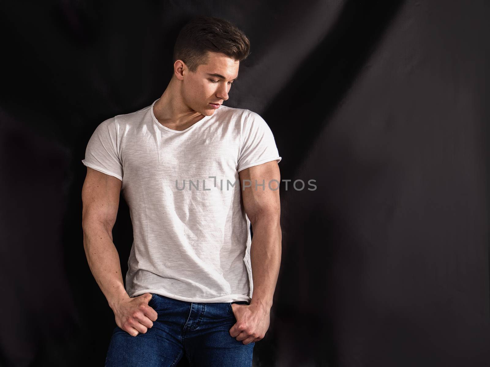 Handsome young muscular man looking down to a side, in studio shot over neutral dark background