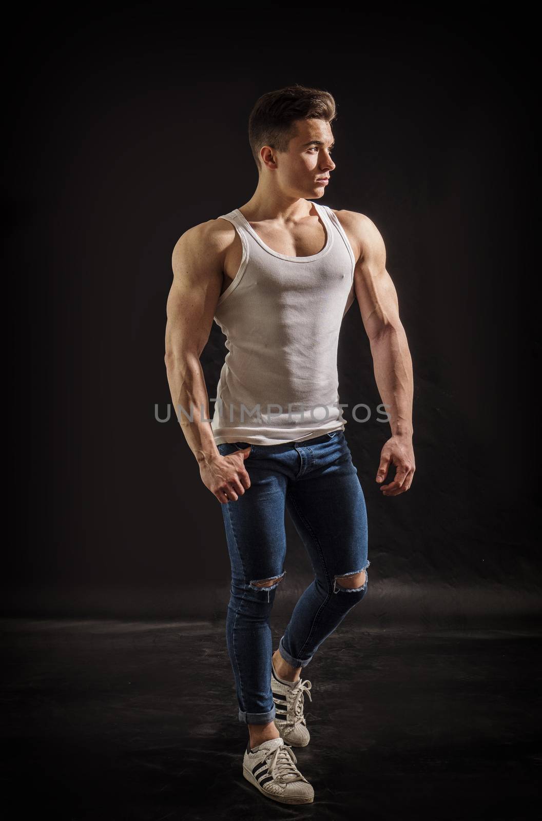 Handsome young muscular man looking to a side, in studio shot over neutral dark background