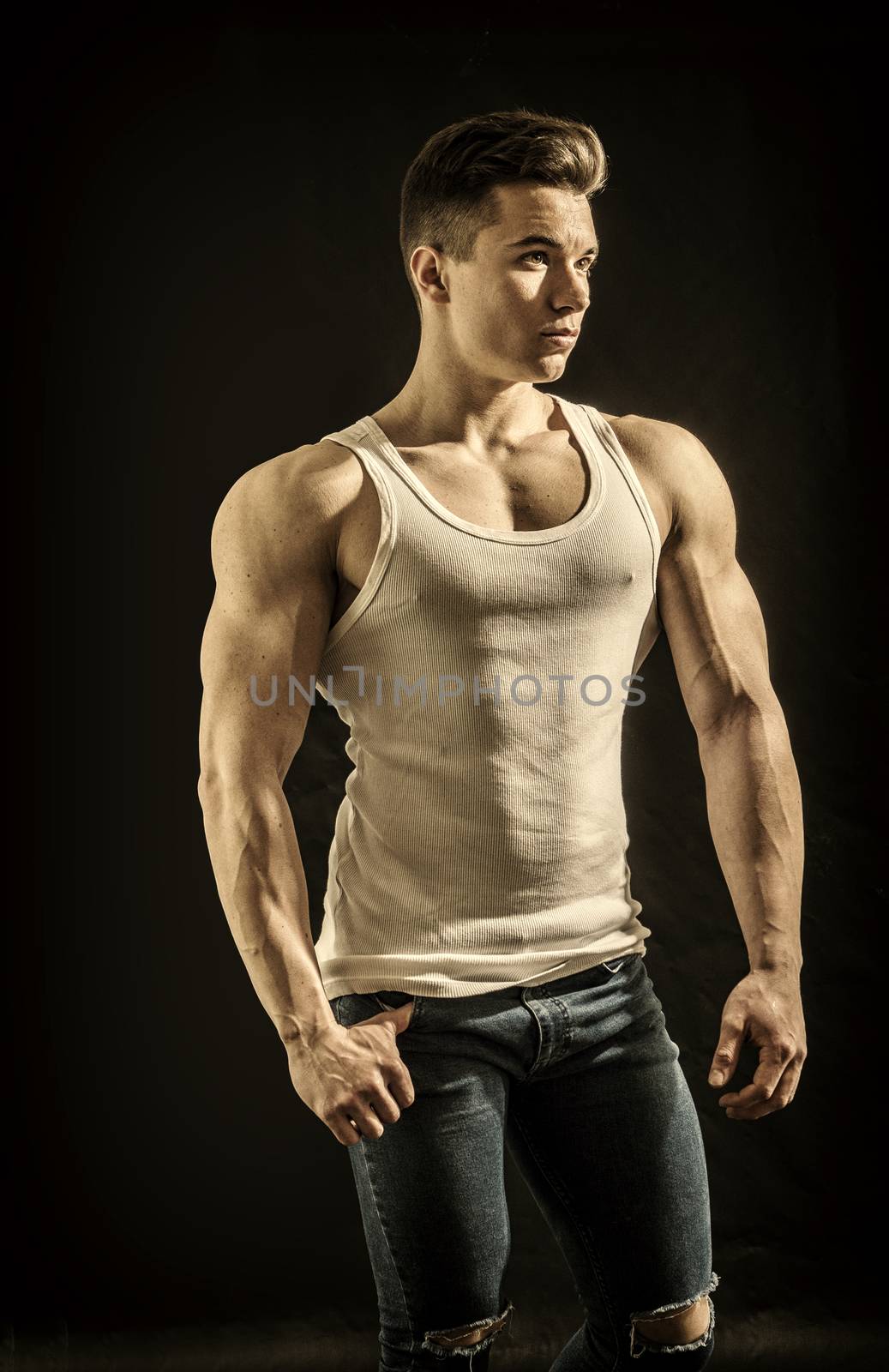 Handsome young muscular man looking to a side, in studio shot over neutral dark background