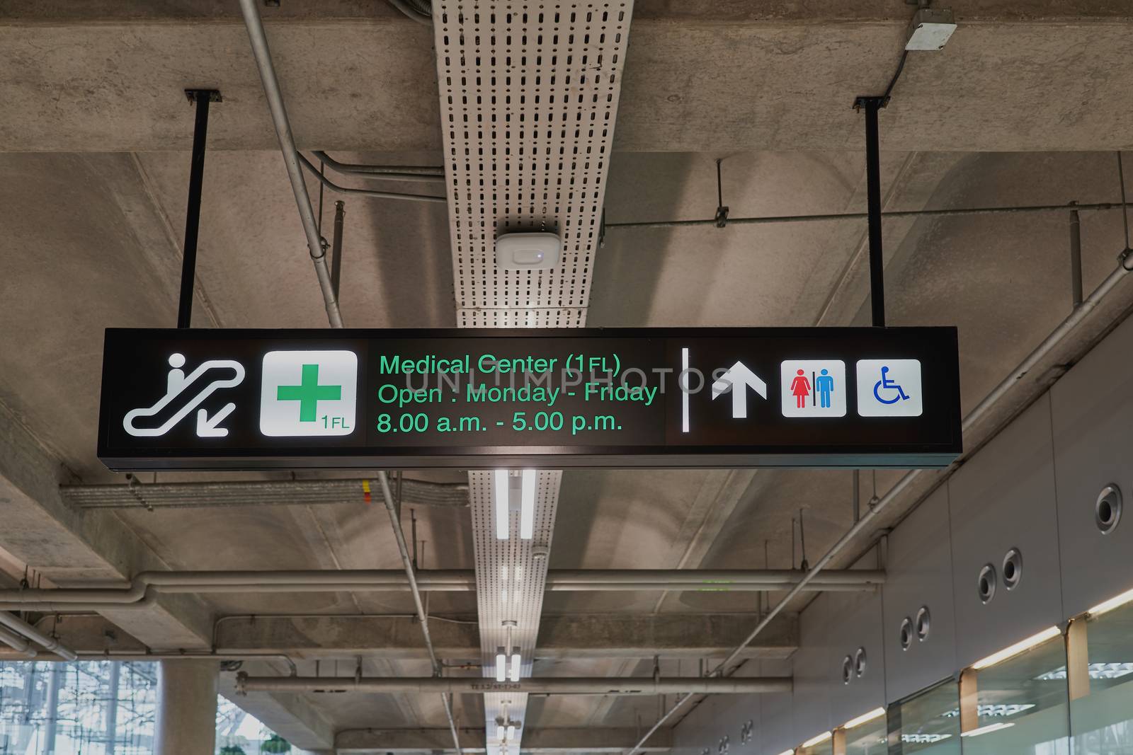 Medical center and toilets information board sign with green character on black background at international airport terminal.