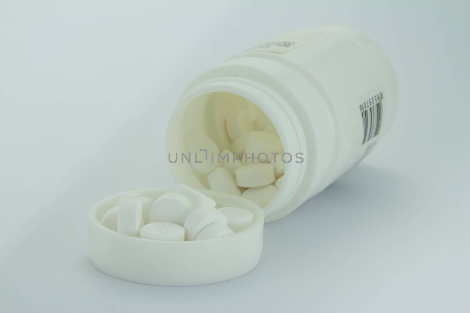 White pills an pill bottle on white background