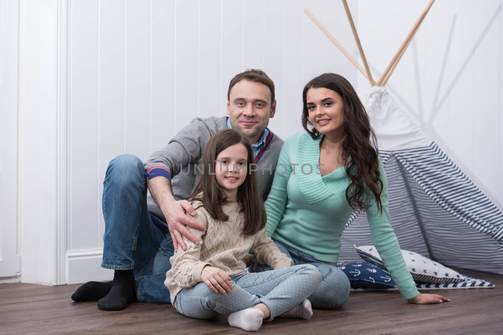 Family portrait of happy parents and their daughter constructed wigwam at home