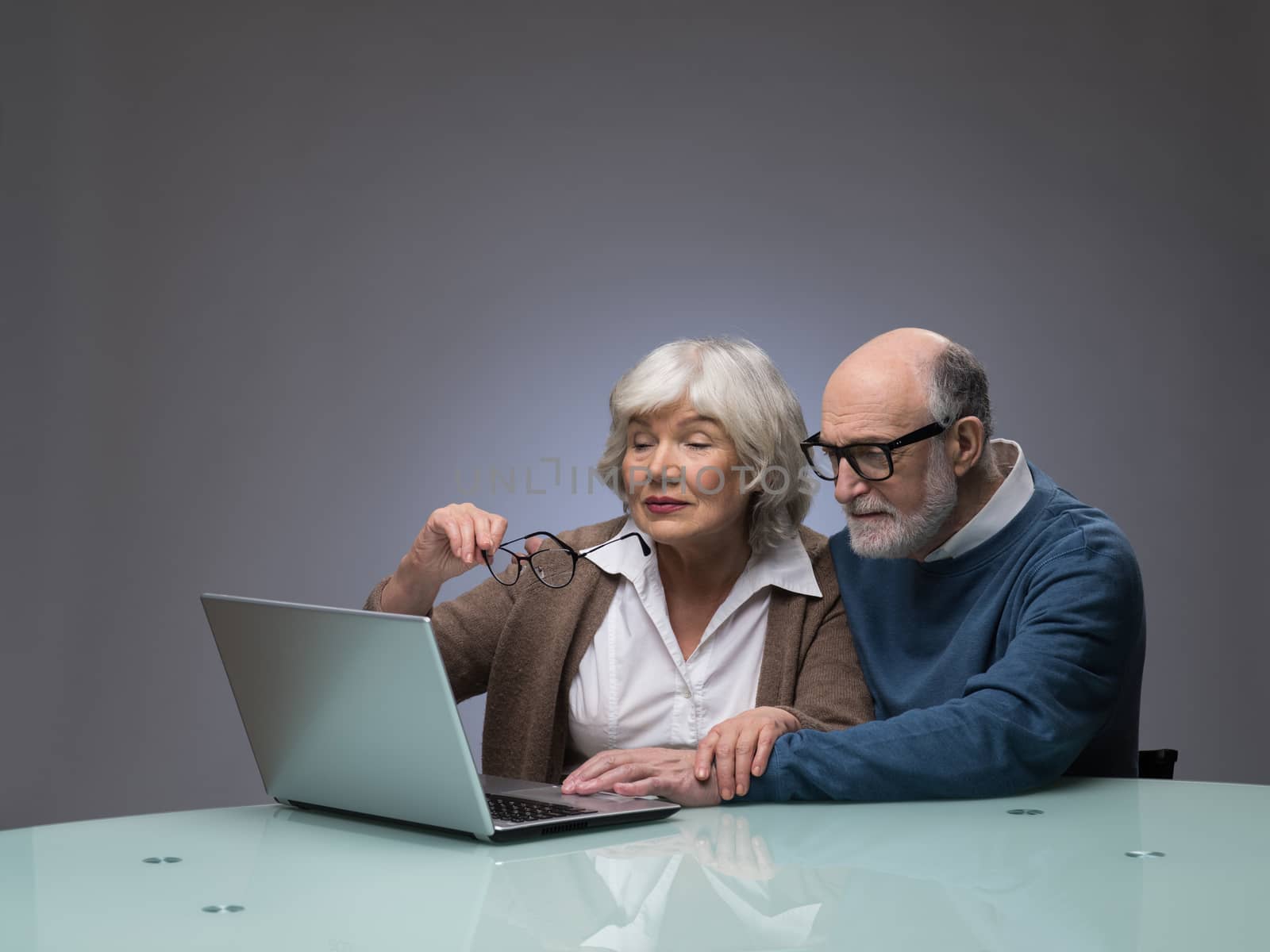 Ssenior couple looking at a laptop together, studio shot on gray background with copy space