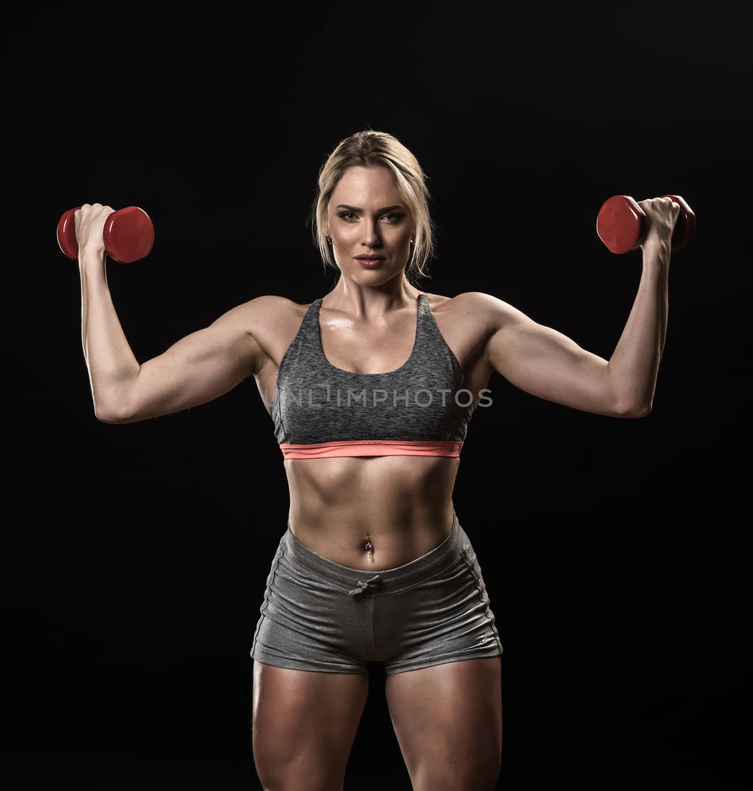Beautiful muscular woman lifting dumbbells isolated on black background