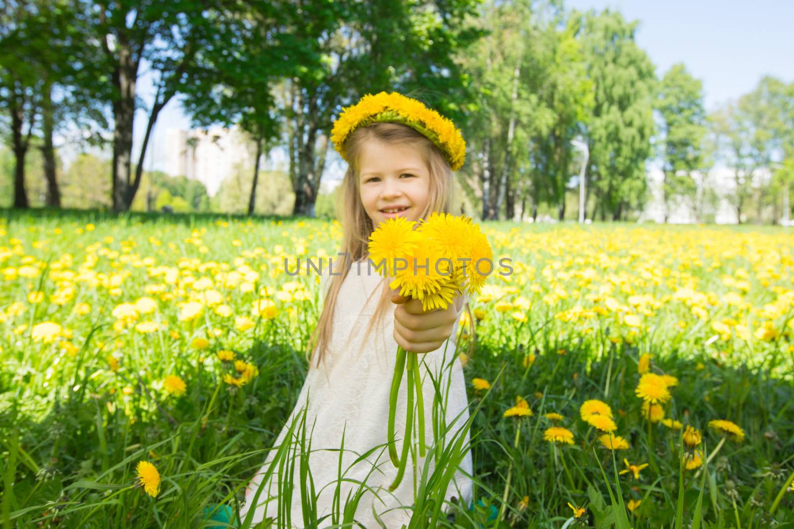 Sweet little girl with floral head wreath on and flowers bunch in hands in summer park
