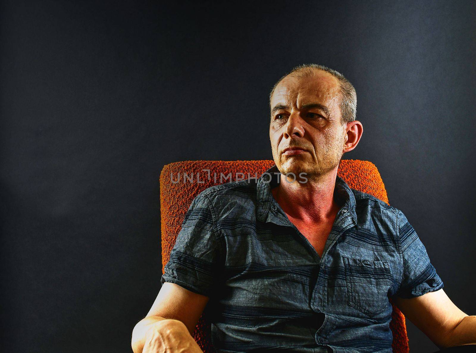 Creative portrai. Middle aged man sitting in an armchair. Portrait of mature man on black background