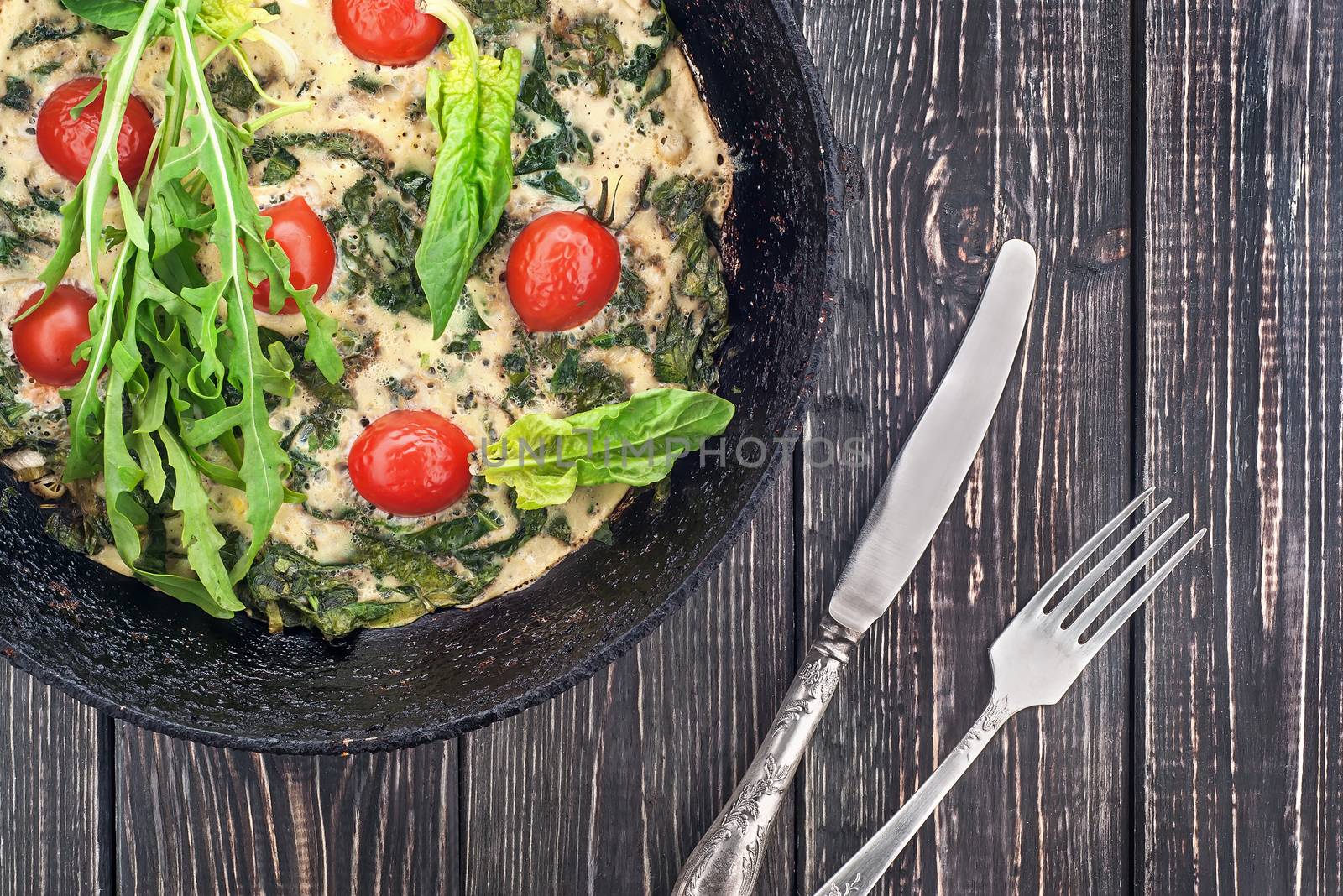 Fritatta in pan with fork and knife. Wooden table top view.