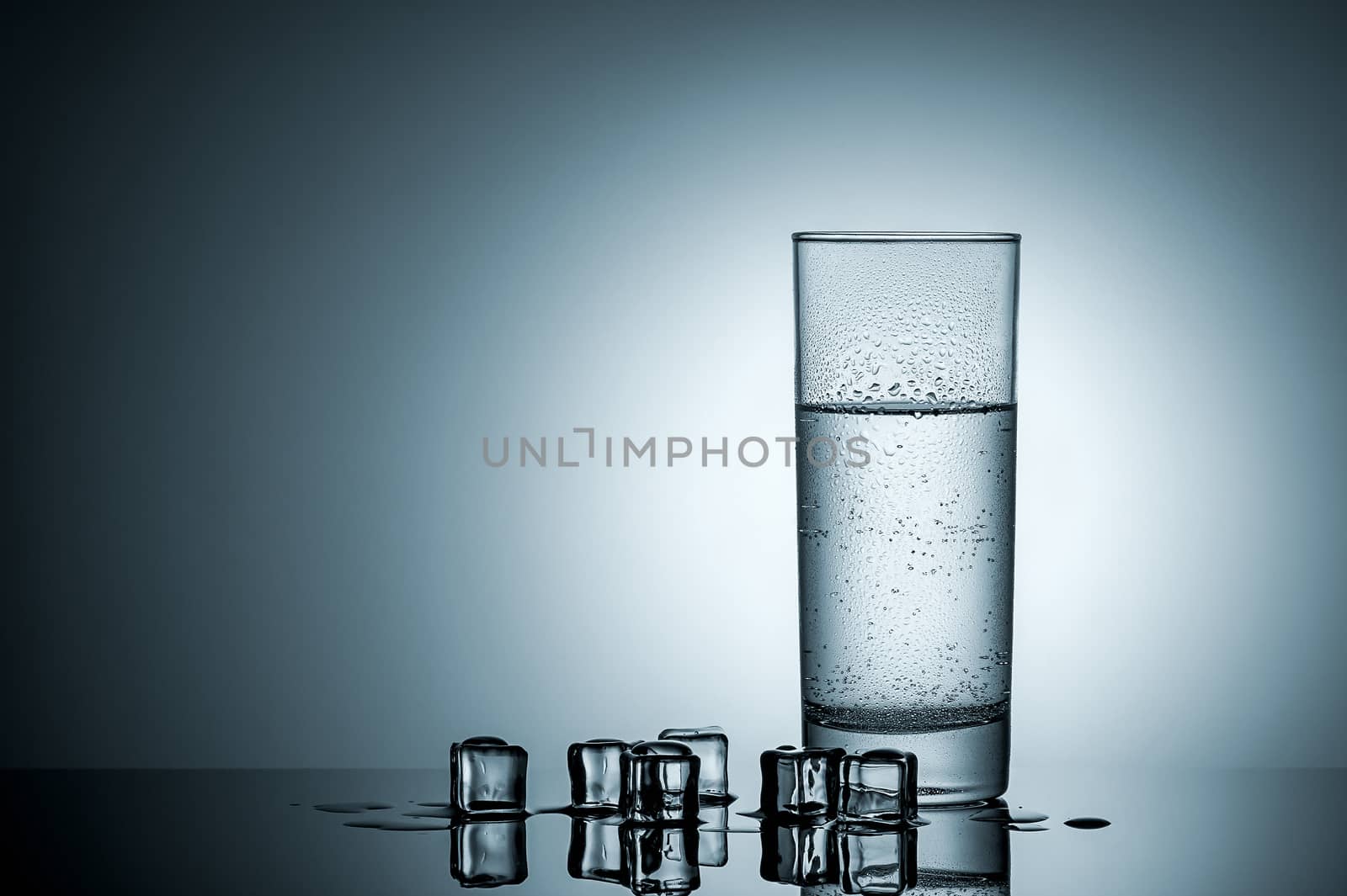 Water in misted glass and ice cubes. Mirror reflection. Gradient background lighting.