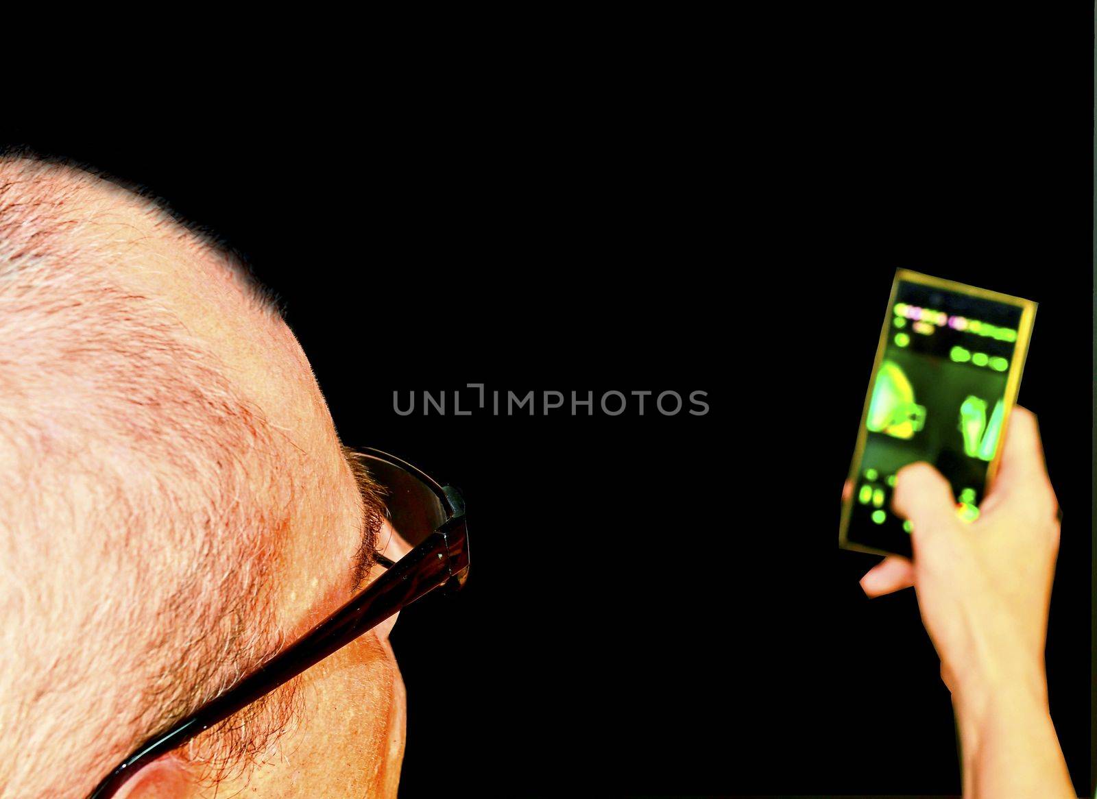 Middle aged man with glasses sitting in an armchair. Mature man with mobile phone on black background. Copy space. Senior concept. 