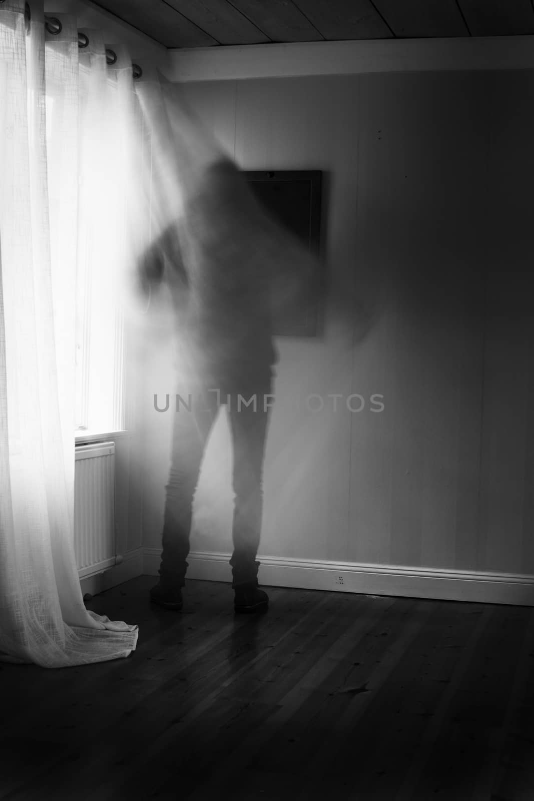 Person in motion blur in front of brightly lit window with curtain, spooky feeling in black and white.