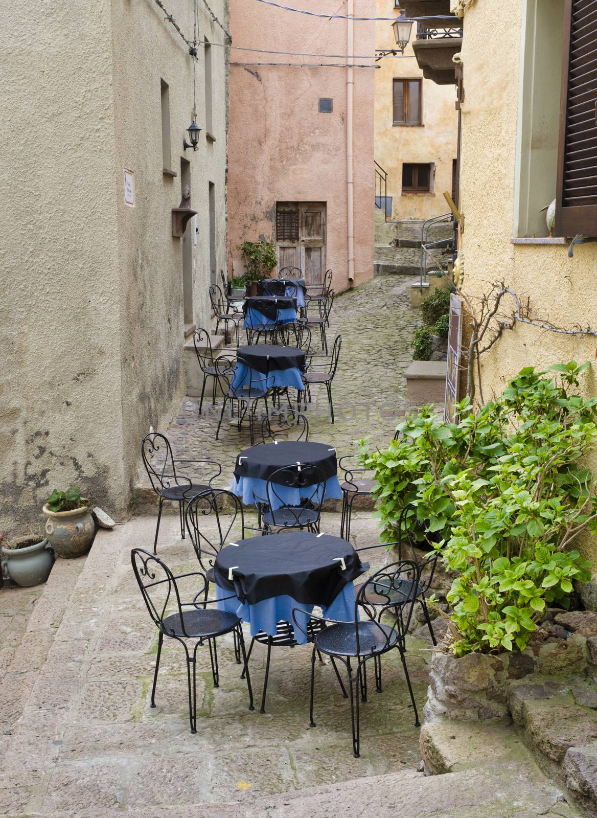 tables with blue cloth and chairs on an outdoor terrace in a street in castelsardo on sardinia