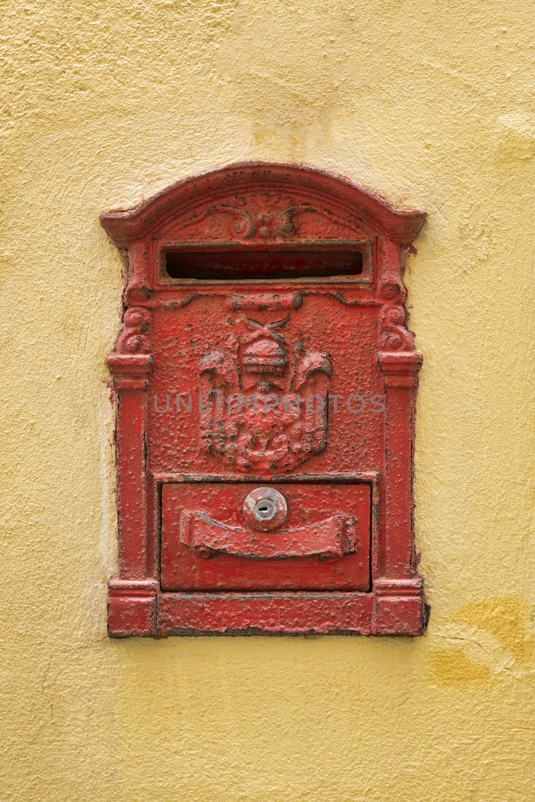 Old red Mailbox  cracked and rusting on yellow wall