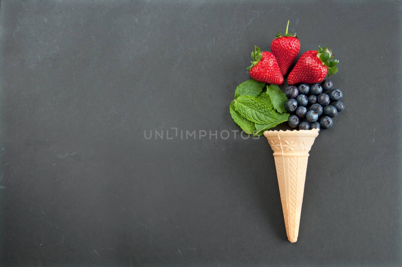 Fresh natural flavors pouring out of an icecream cone including strawberry, mint and blueberries