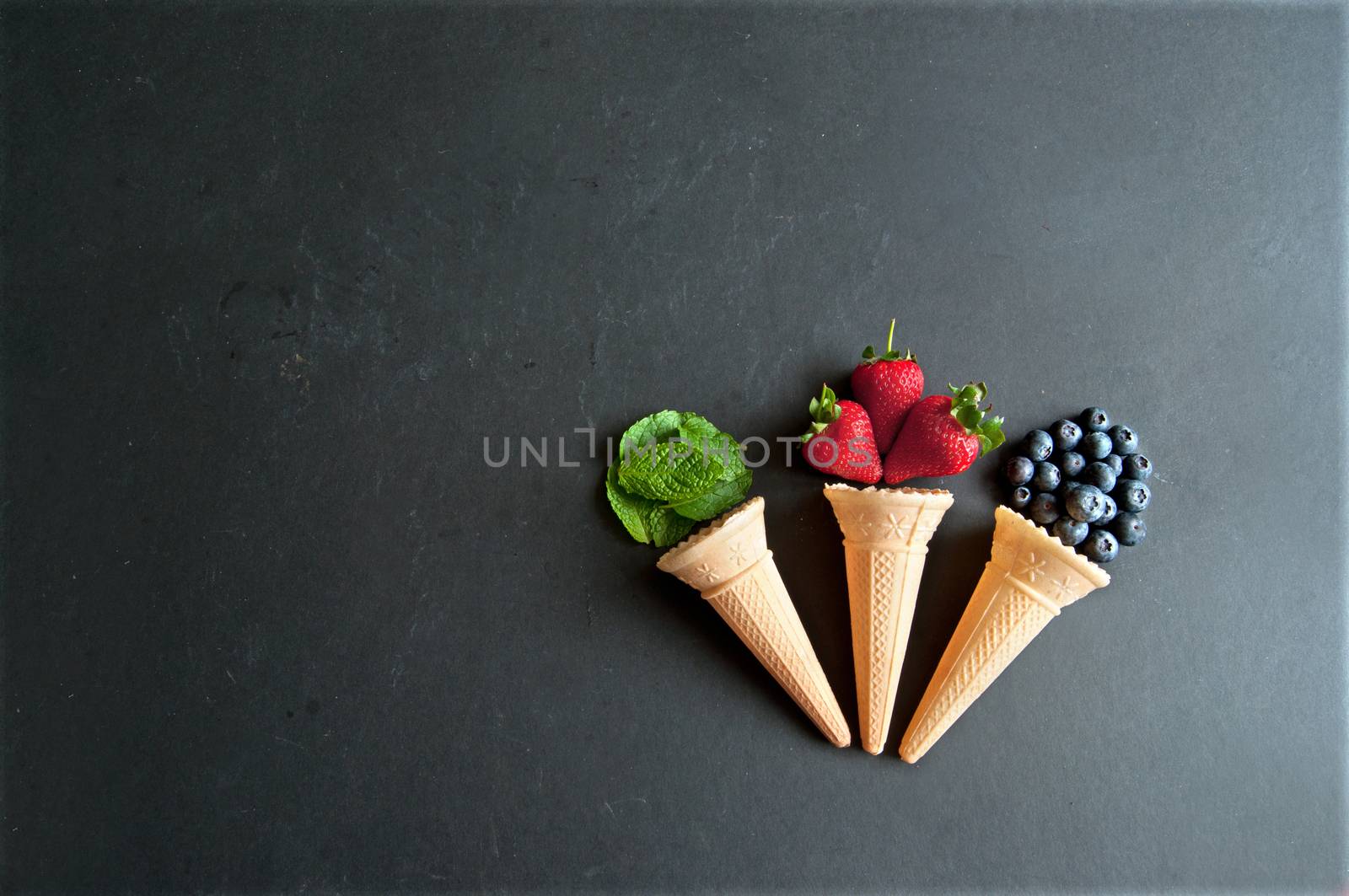 Natural ingredients spilling out of an icecream cones including strawberry, mint and blueberry flavors