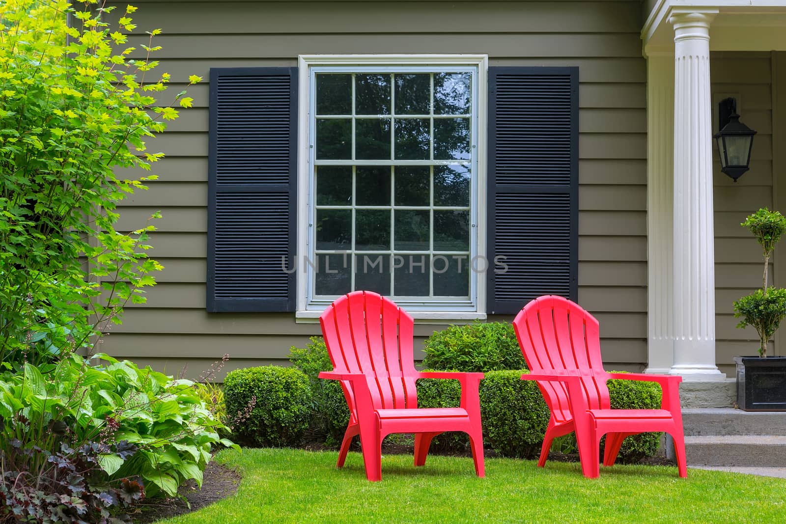 Red outdoor chairs on green grass lawn of house manicured front yard
