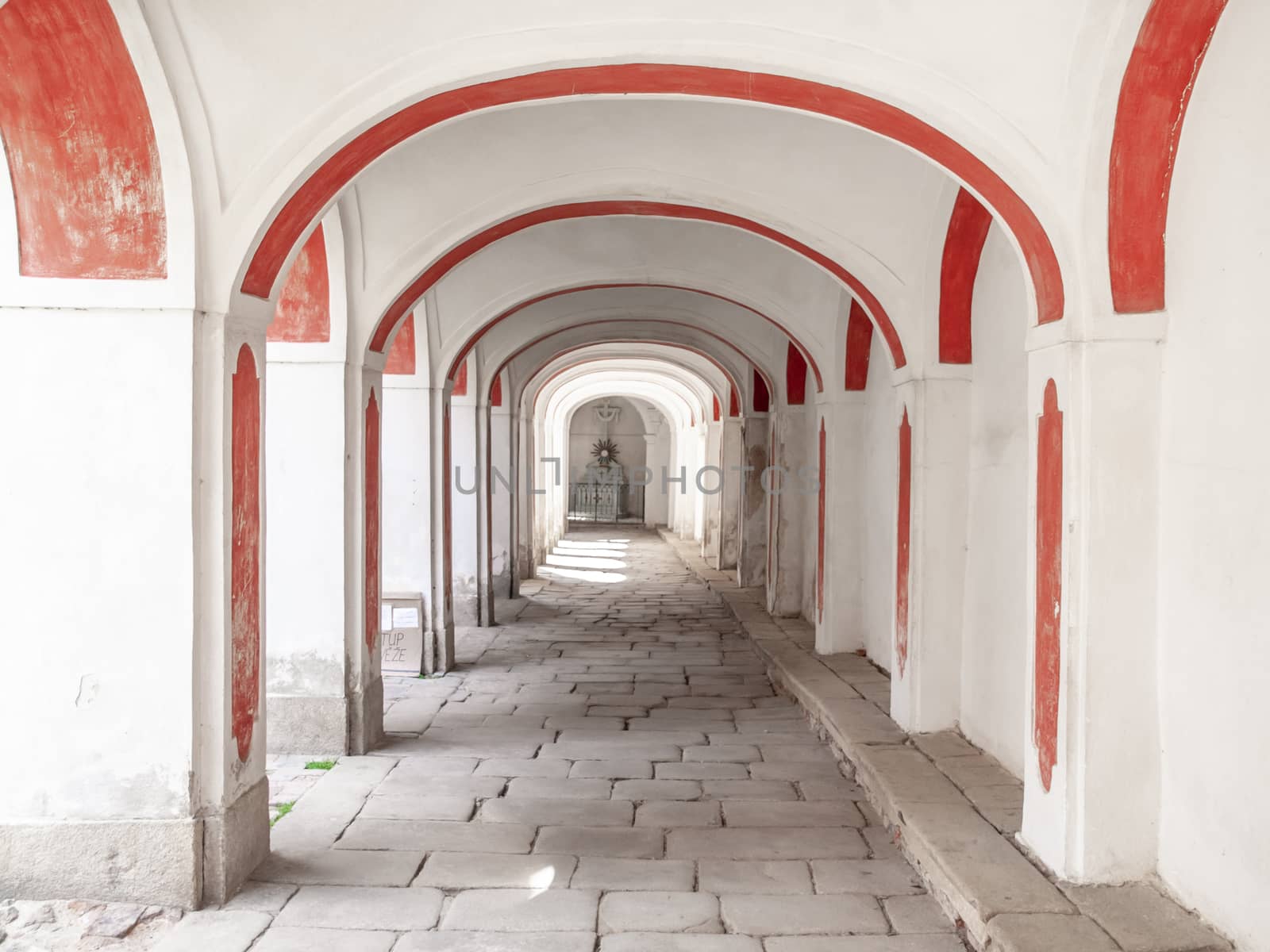 Long arcade corridior with white and red facade and cobbled floor.