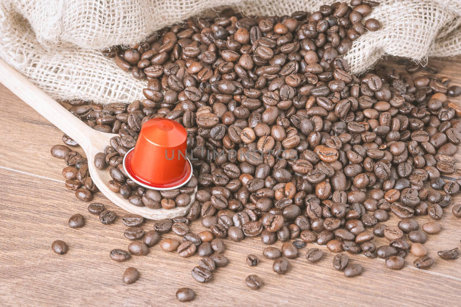 Coffee capsule on wooden spoon and  roasted coffee beans with burlap sack on wooden background.