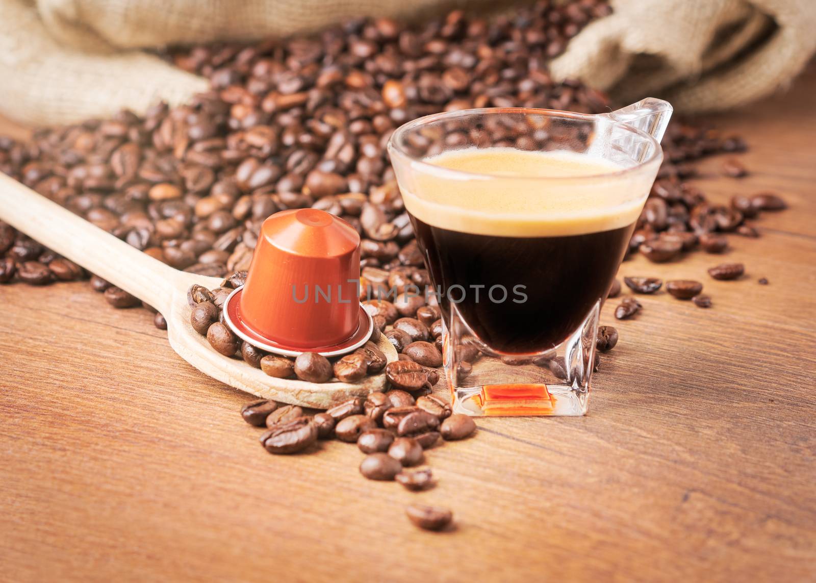 Cup of coffee with coffee capsule on wooden spoon, roasted coffee beans on wooden background,front view.