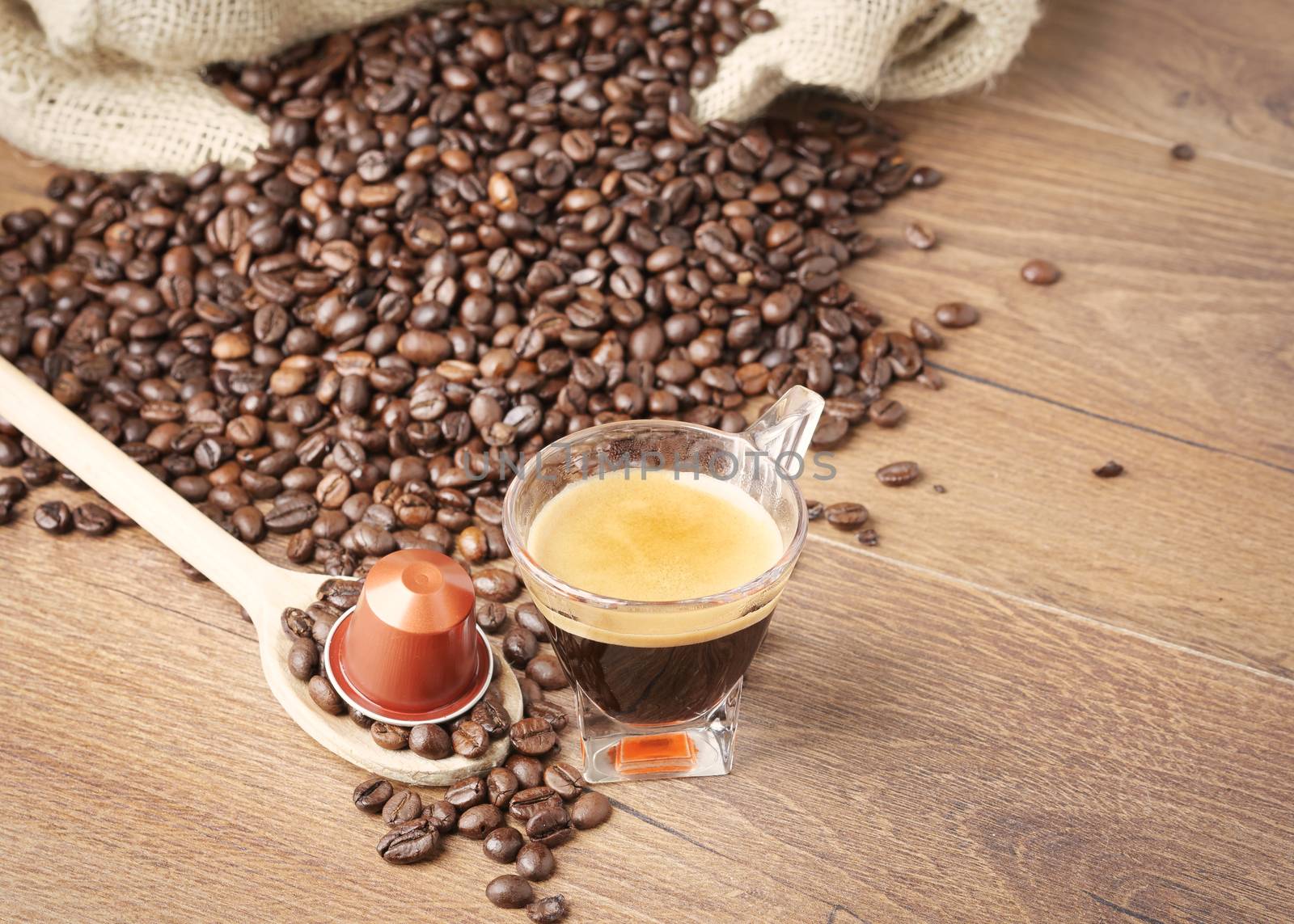 Cup of coffee with coffee capsule on wooden spoon, roasted coffee beans on wooden background,top view.