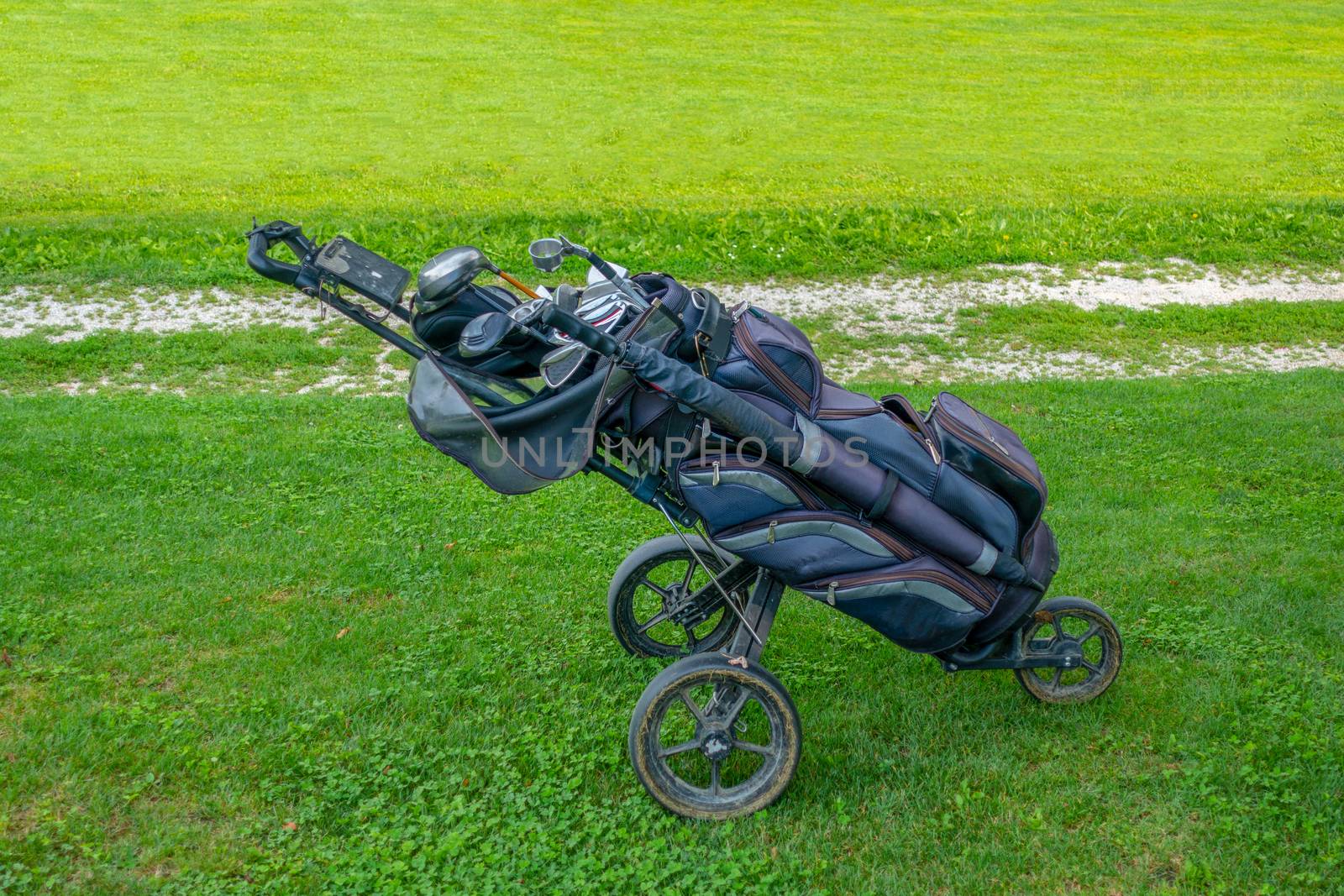 Golf bag with clubs on roller stand on golf course, authentic, not staged, after plaz with muddy wheels