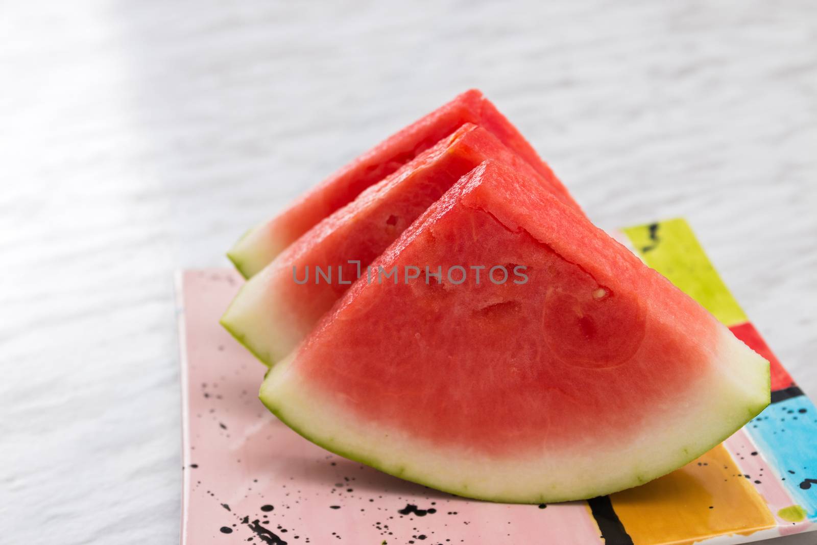 Slices of juicy watermelon on a bright ceramic plate, on marble background.