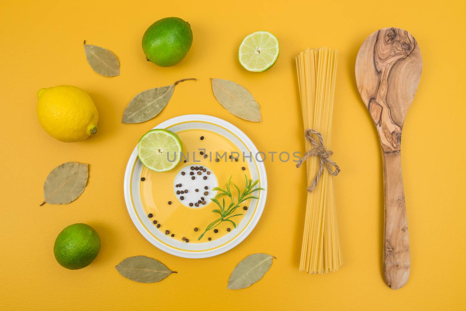Cooking ingredients on bright yellow background. Limes, lemons, laurel leaves, pasta and spices.