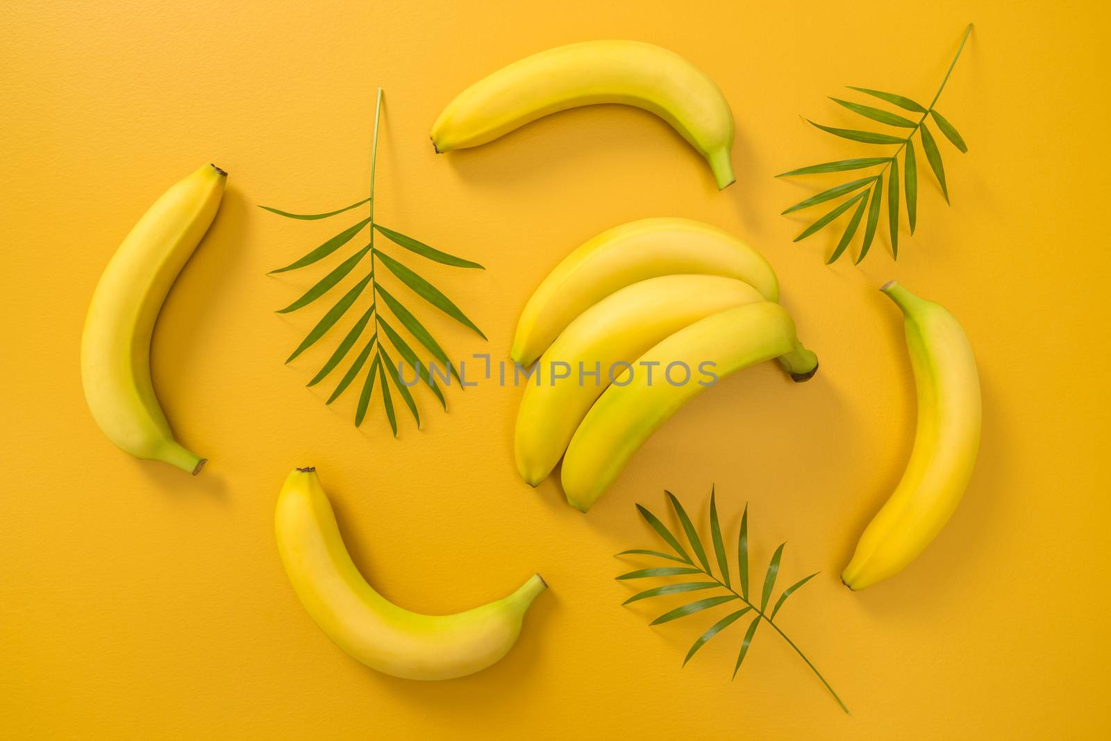 Bananas and palm leaves on vibrant yellow background. Tropical summer theme.