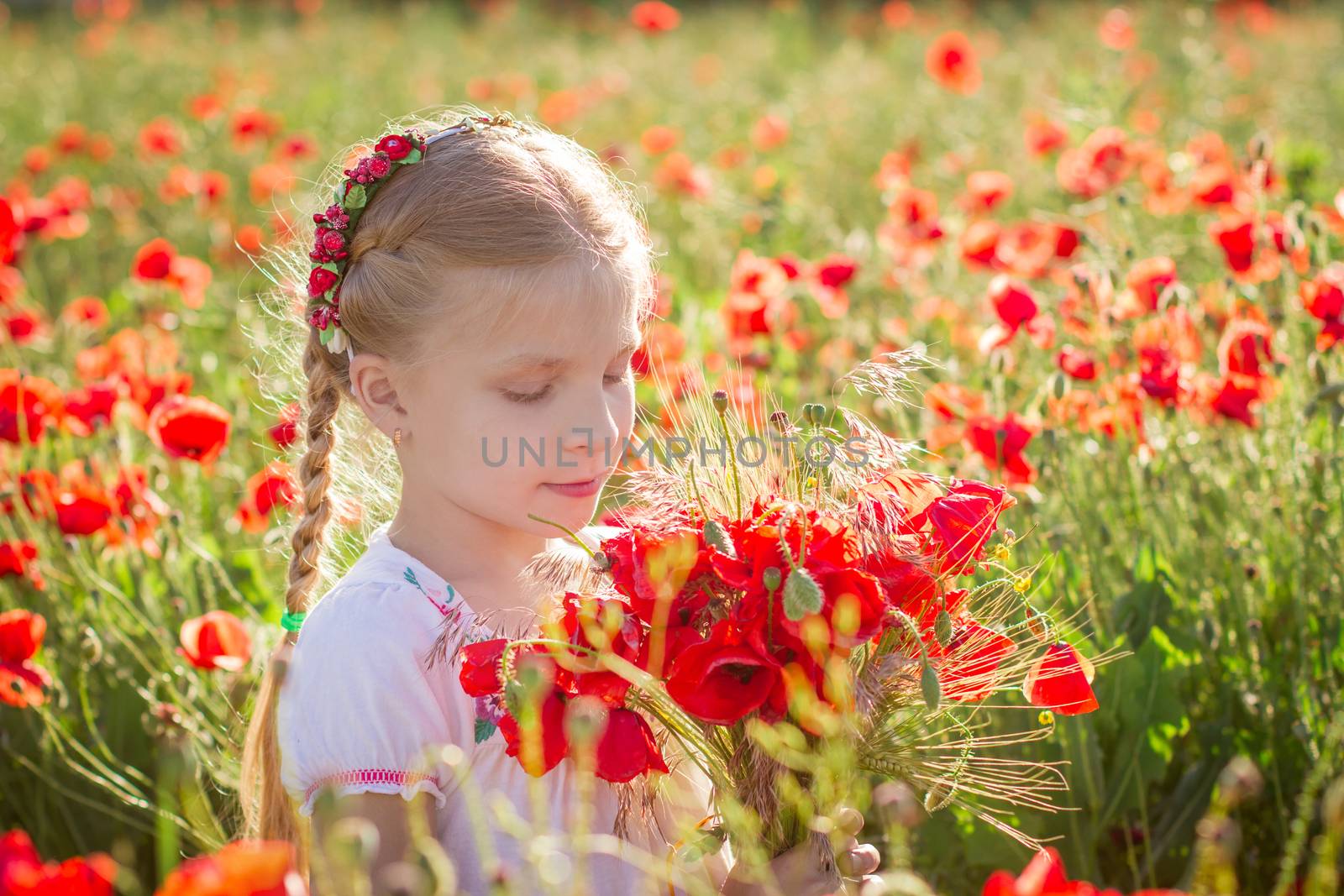 Young girl with bouquet among poppies field at sinset