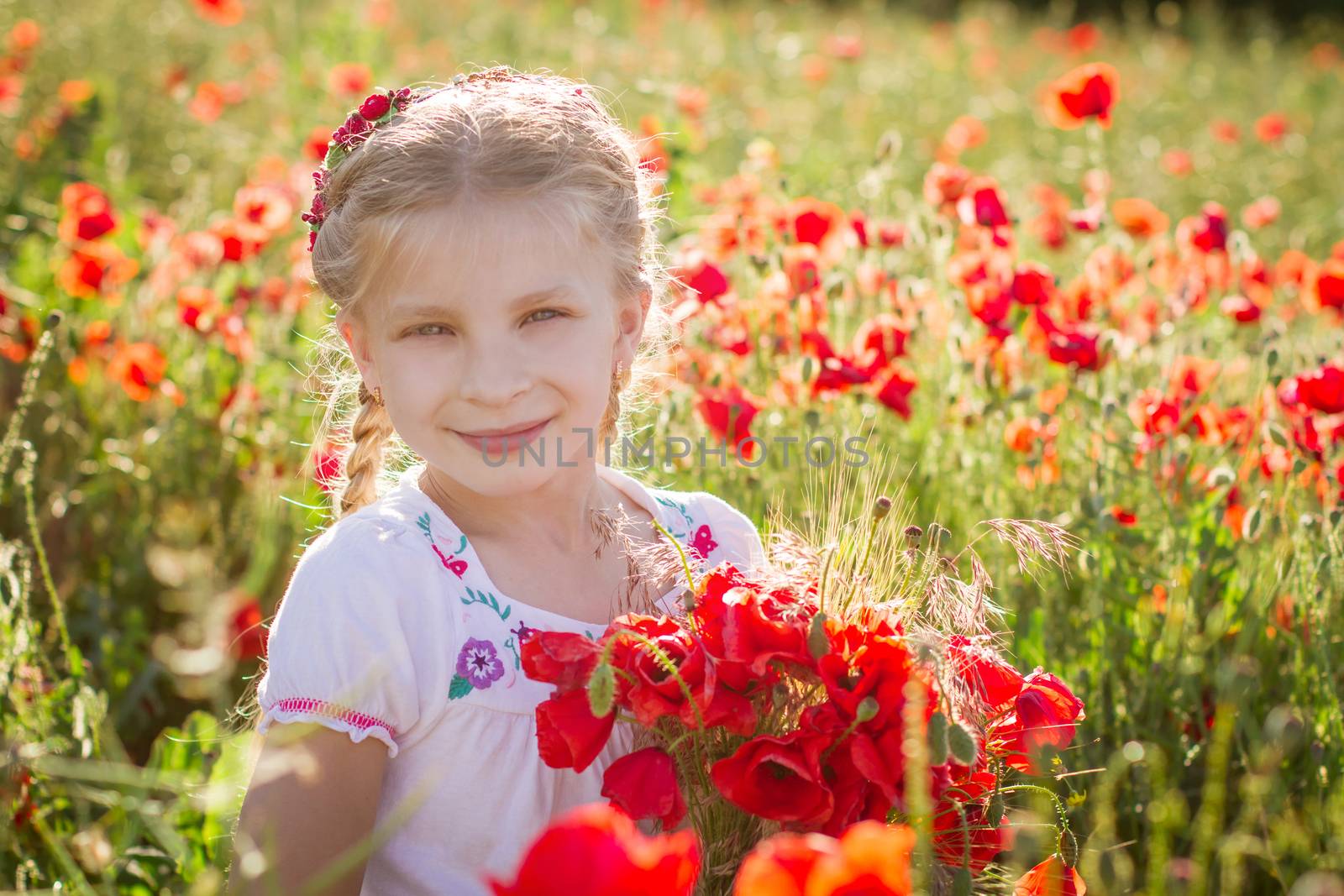 young girl with bouquet among poppies field at sunset