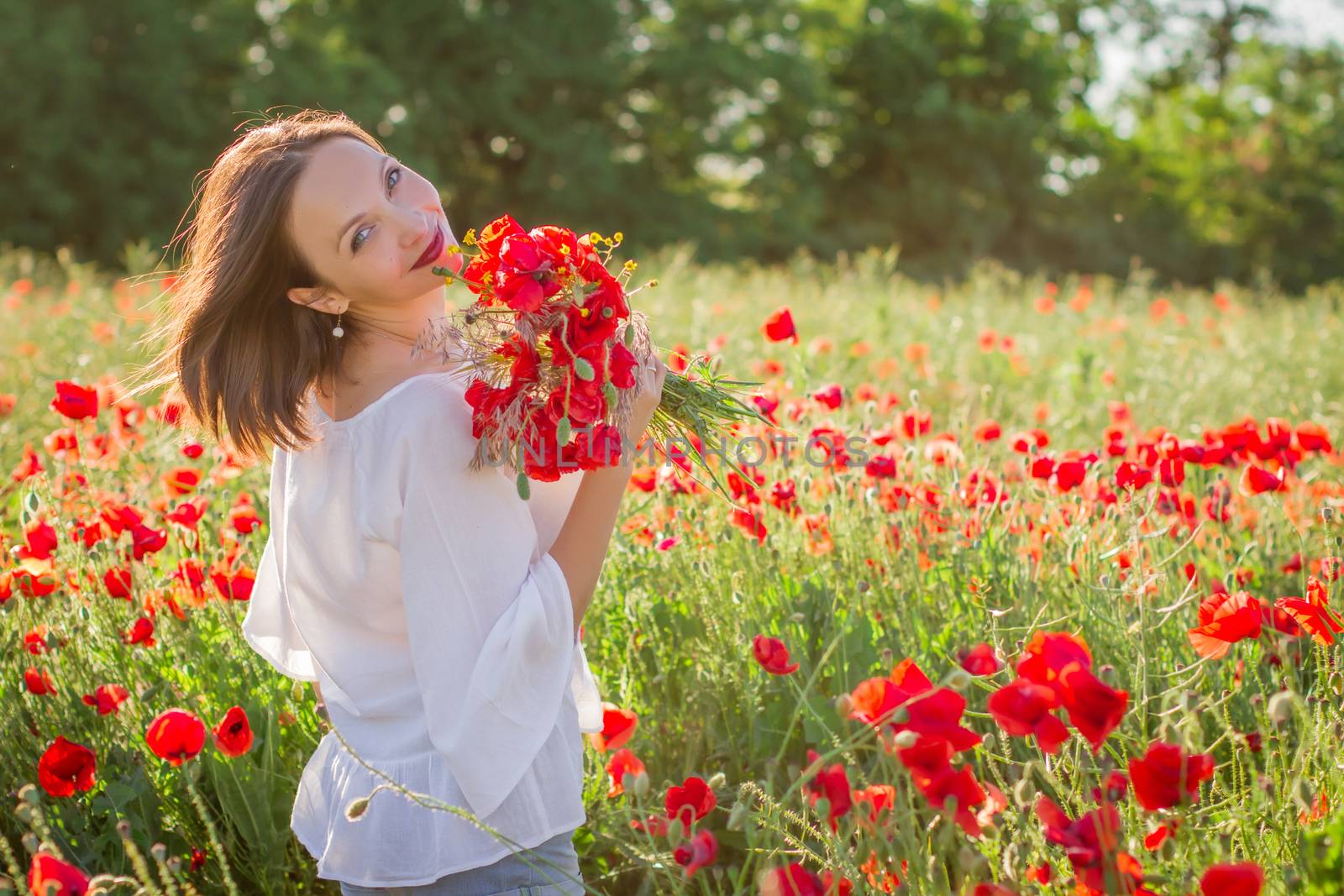 Woman with bouquet among poppies field at sunset