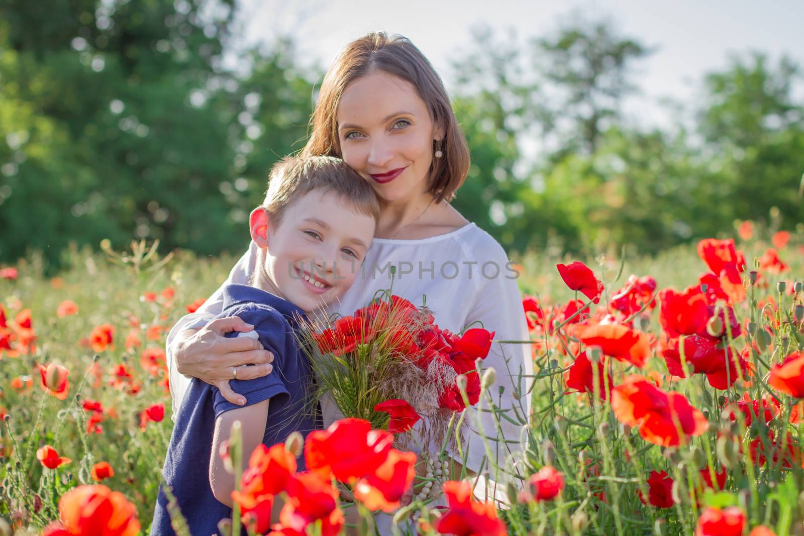 Mother in white with son holding bouquet on blossoming red poppies field by Angel_a