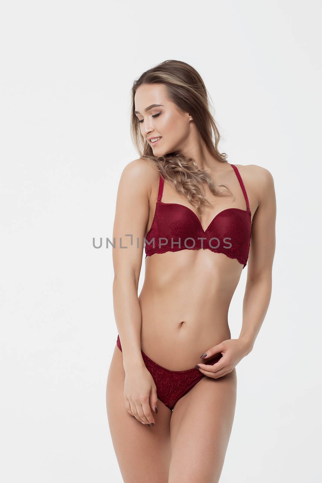 Seductive young woman in red underwear touching breast on white background