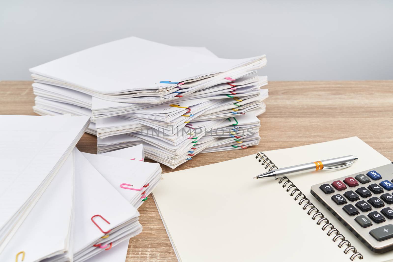 Pen on notebook with calculator have overload paperwork report of sale and receipt with colorful paper clip on wooden table with white background and copy space. Business and finance concept success.