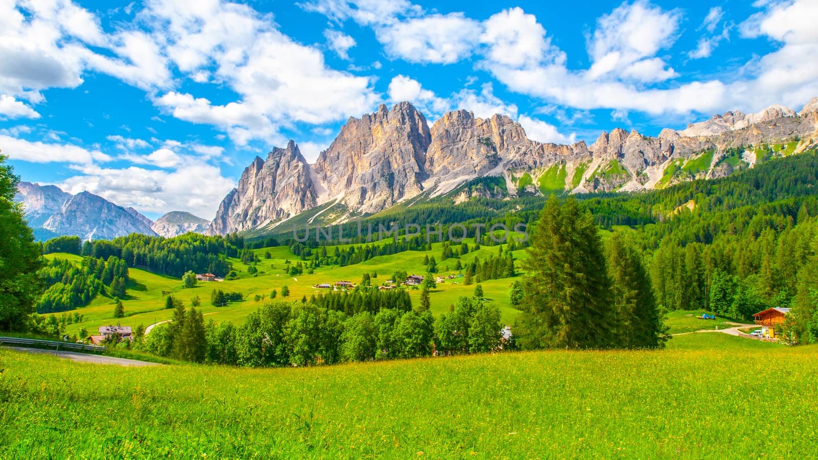 Rocky ridge of Pomagagnon Mountain above Cortina d'Ampezzo with green meadows and blue sky with white summer clouds, Dolomites,, Italy by pyty